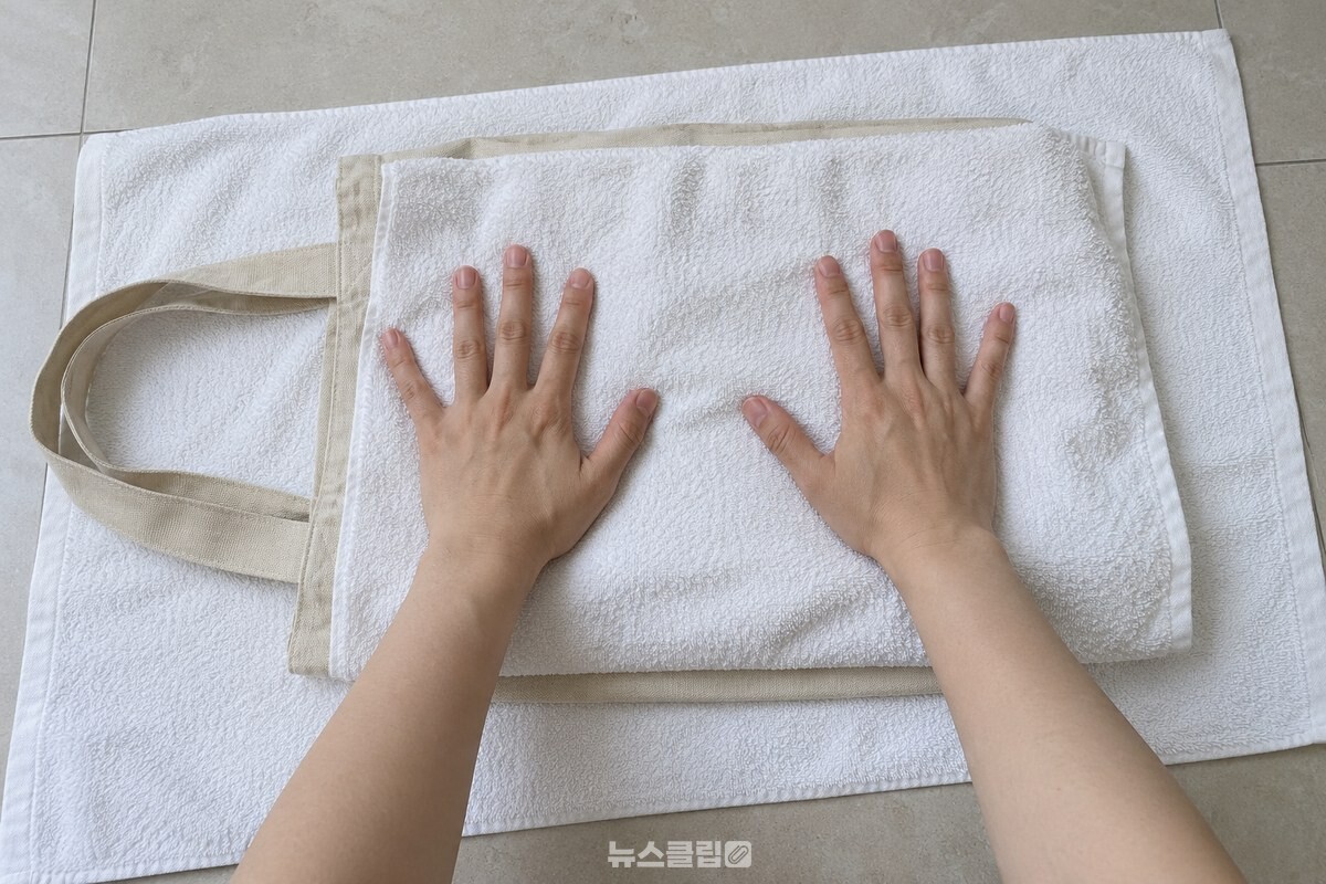 마른 수건 사이에 놓은 천 가방을 손바닥으로 눌러 물기를 빼는 모습. / 기사 이해를 돕기 위한 생성형 이미지