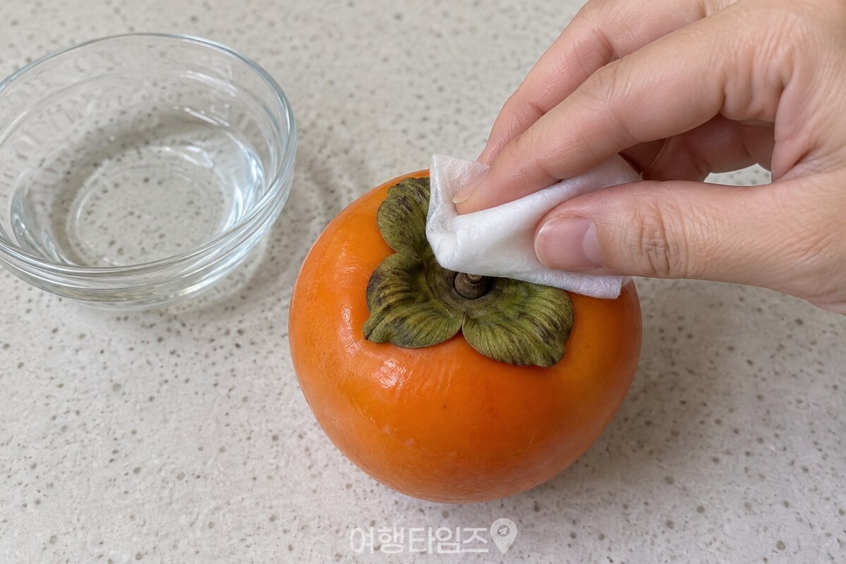촉촉하게 짠 화장솜을 단감 꼭지 위에 밀착시키는 손 / 기사 이해를 돕기 위한 생성형 이미지