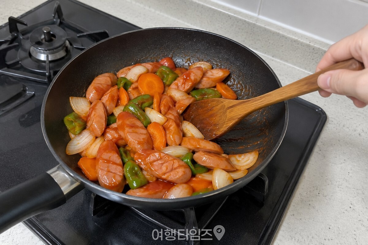 케첩을 넣은 뒤 소시지와 채소에 소스가 고루 묻도록 팬에서 가볍게 섞고 있다. / 기사 이해를 돕기 위한 생성형 이미지
