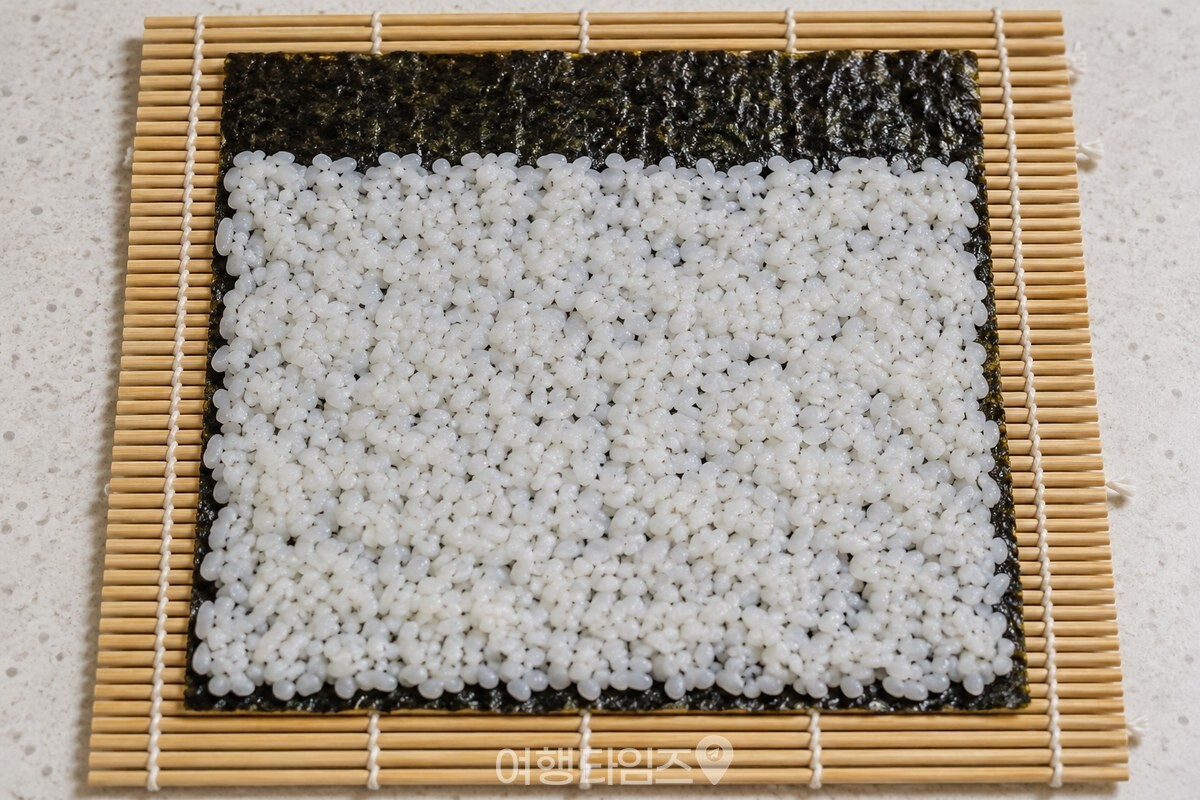 김발 위 김에 밥을 얇고 고르게 펴고 윗부분을 남겨 둔 모습. / 기사 이해를 돕기 위한 생성형 이미지