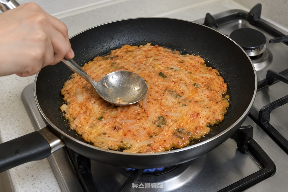 검은 프라이팬 가장자리에서 반죽을 얇고 둥글게 펴 부치는 장면이다. / 기사 이해를 돕기 위한 생성형 이미지