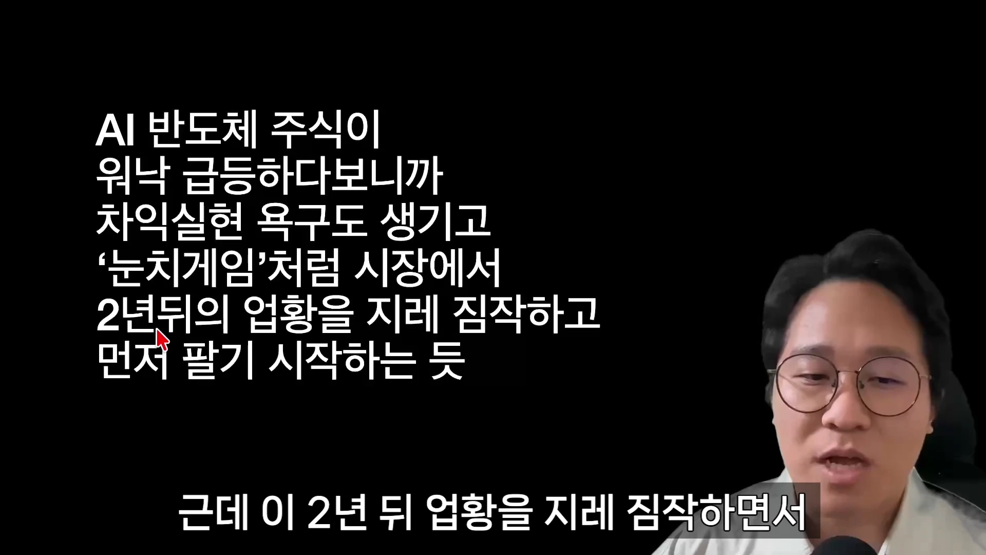 안경을 쓴 남성이 검은색 배경에 흰색 자막이 적힌 영상 화면 옆에서 설명하고 있다.