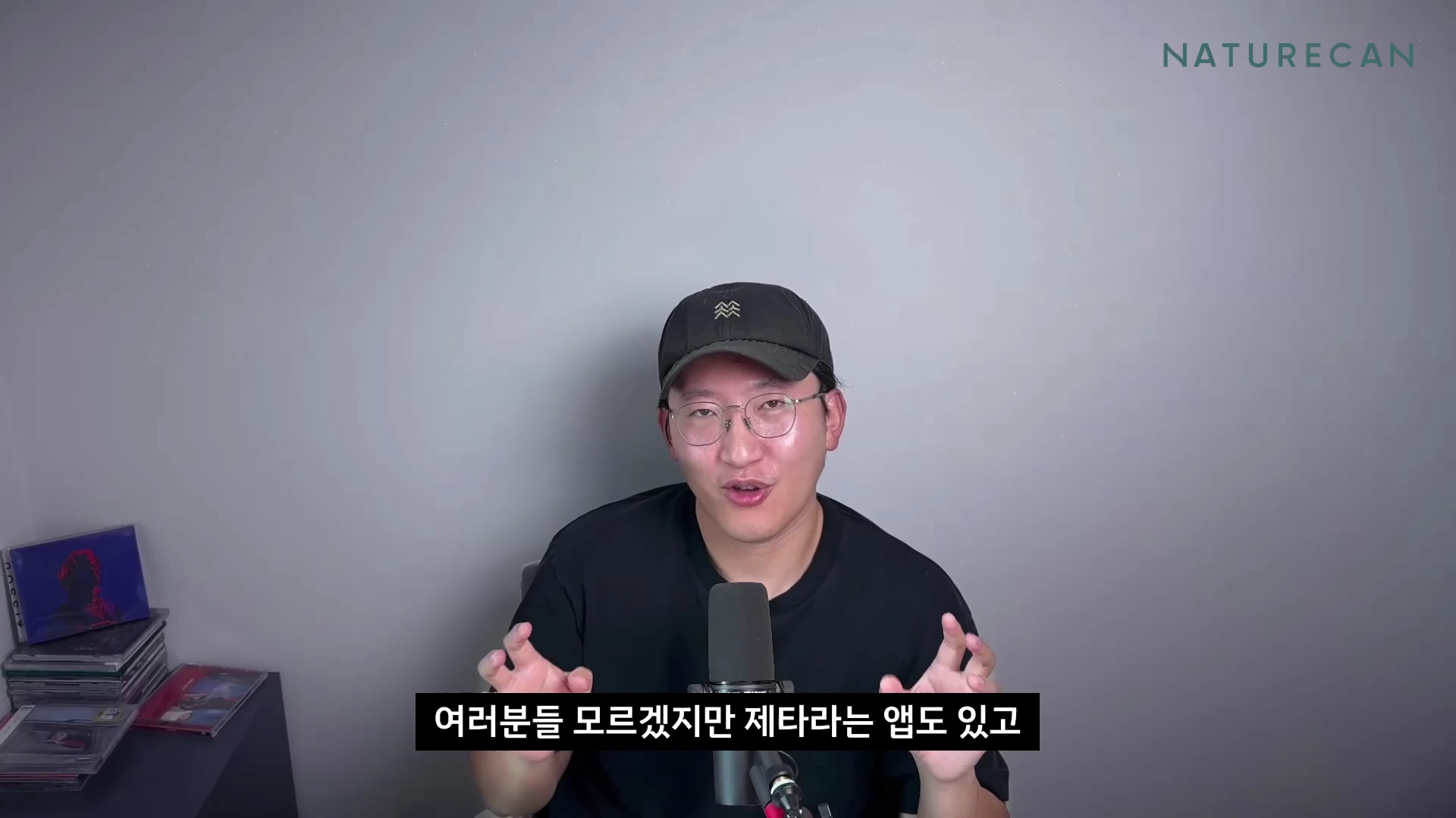 검은색 모자와 안경을 쓴 남성이 마이크 앞에 앉아 손짓하며 이야기를 나누고 있는 모습이 담긴 영상 캡처 화면입니다.