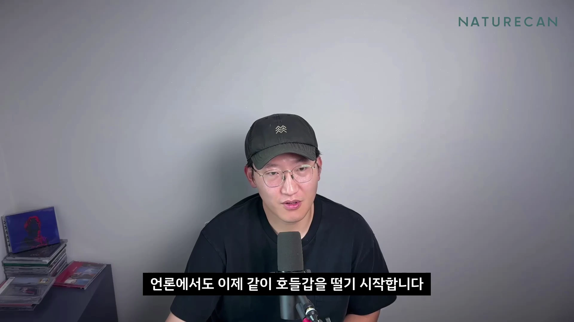 검은색 모자와 안경을 쓴 남성이 마이크 앞에 앉아 정면을 바라보며 이야기하고 있다.