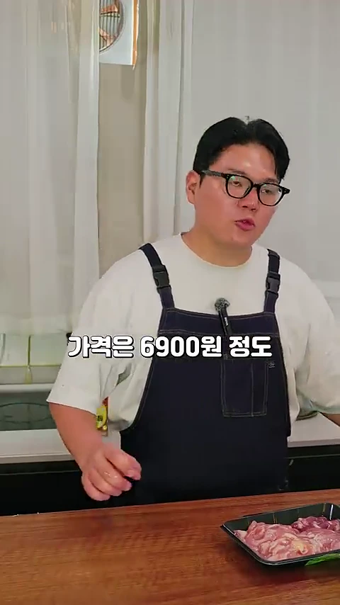 안경을 쓴 요리사가 흰색 티셔츠에 앞치마를 두르고 주방 테이블 앞에 서 있으며, 옆에는 생닭 특수부위가 담긴 플라스틱 팩이 놓여 있습니다. 화면 중앙에는 '가격은 6900원 정도'라는 자막이 표시되어 있습니다.