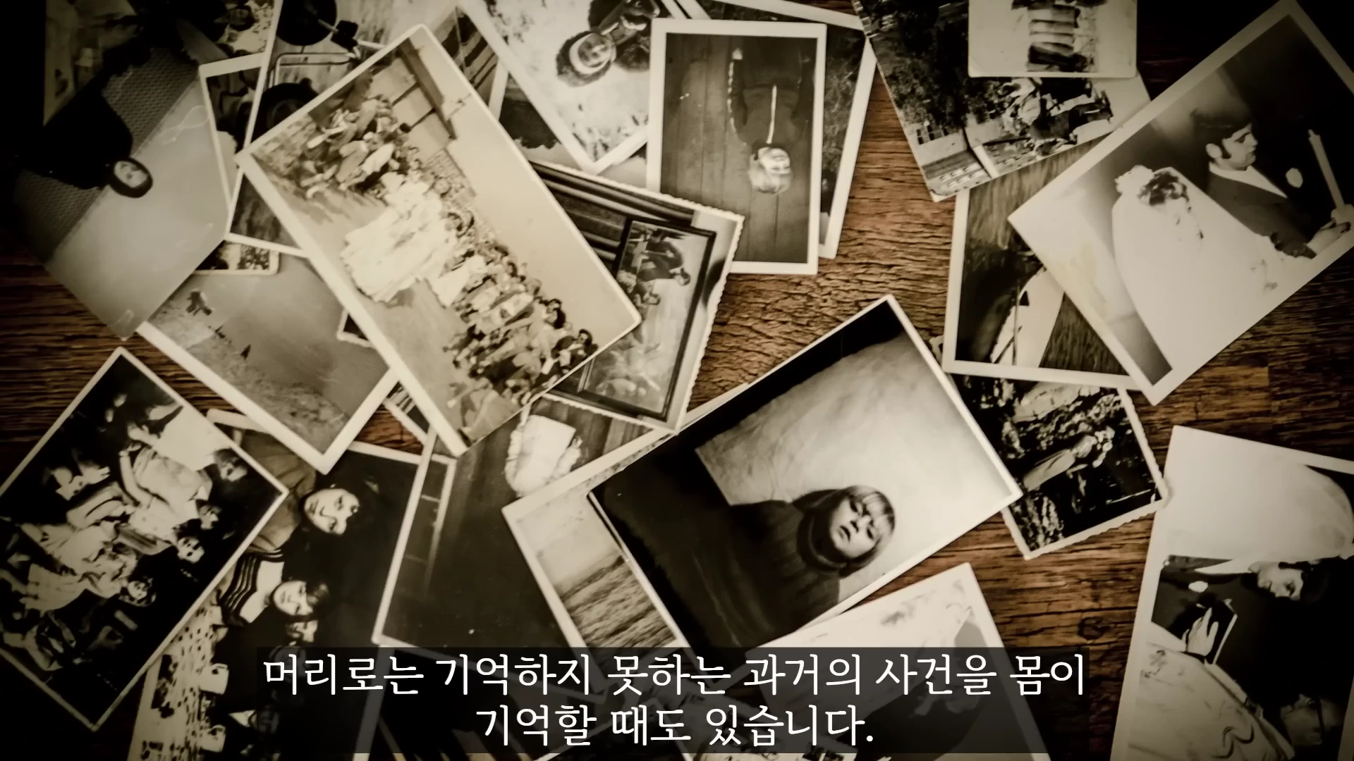 나무 바닥 위에 흑백 사진들이 무작위로 겹쳐져 흩어져 있는 모습으로, 사람들의 일상적인 모습이 담긴 여러 장의 사진이 배치되어 있다.