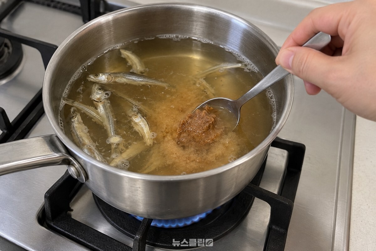 국멸치를 볶은 냄비의 맑은 국물에 된장 한 큰술을 숟가락으로 풀고 있다. / 기사 이해를 돕기 위한 생성형 이미지