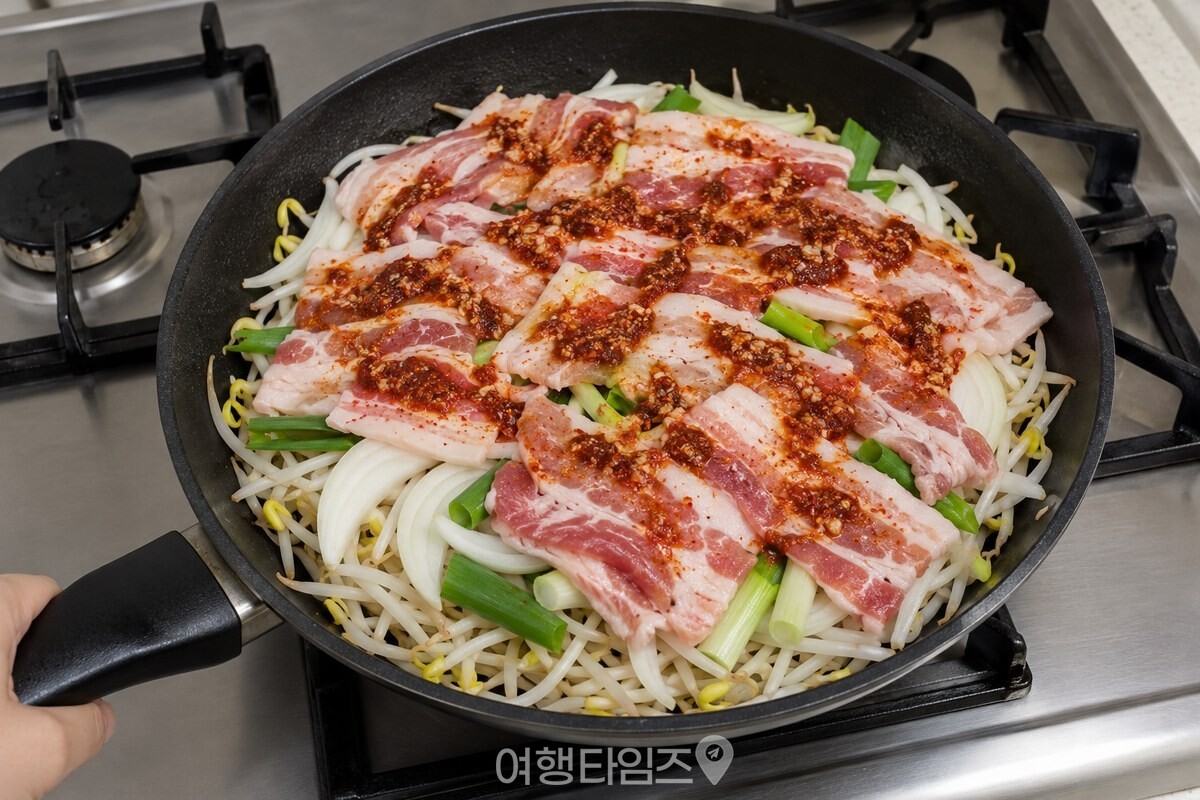 콩나물 위에 채소와 대패삼겹살, 양념을 층층이 올린 팬. / 기사 이해를 돕기 위한 생성형 이미지