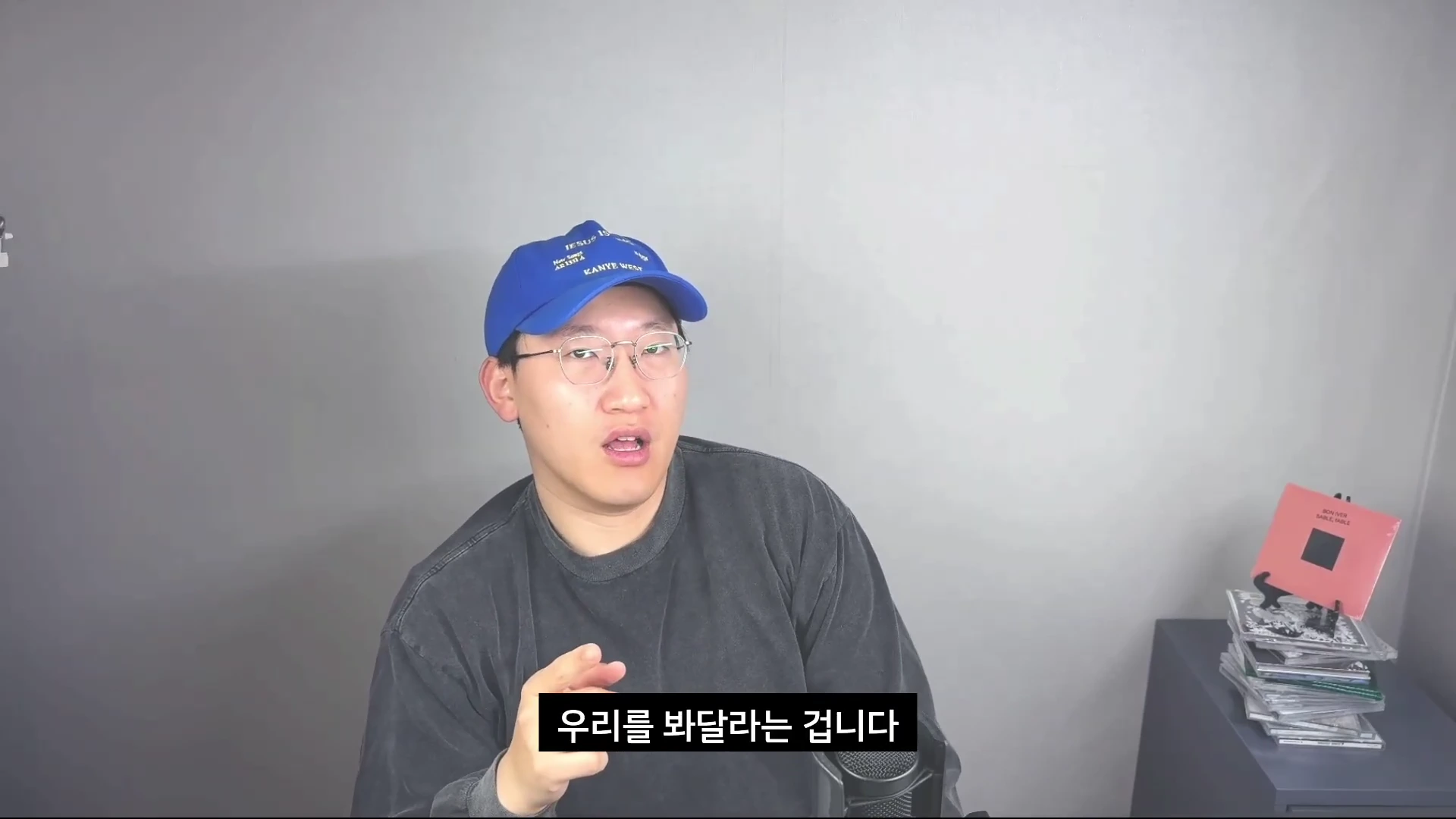 파란색 야구 모자를 쓰고 안경을 쓴 남성이 마이크 앞에서 이야기하고 있으며, 화면 하단에는 '우리를 봐달라는 겁니다'라는 자막이 표시되어 있다.