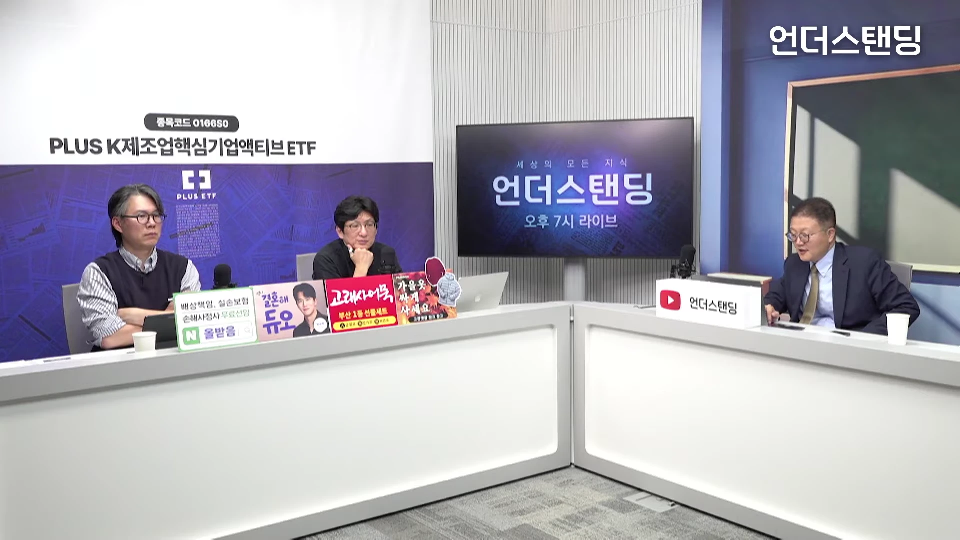 두 명의 남성이 책상 앞에 앉아 대화를 나누고 있는 스튜디오 세트장이며, 한 남성은 오른편의 다른 책상에 홀로 앉아 있습니다. 배경에는 '언더스탠딩' 로고가 적힌 대형 화면과 광고 패널들이 설치되어 있습니다.