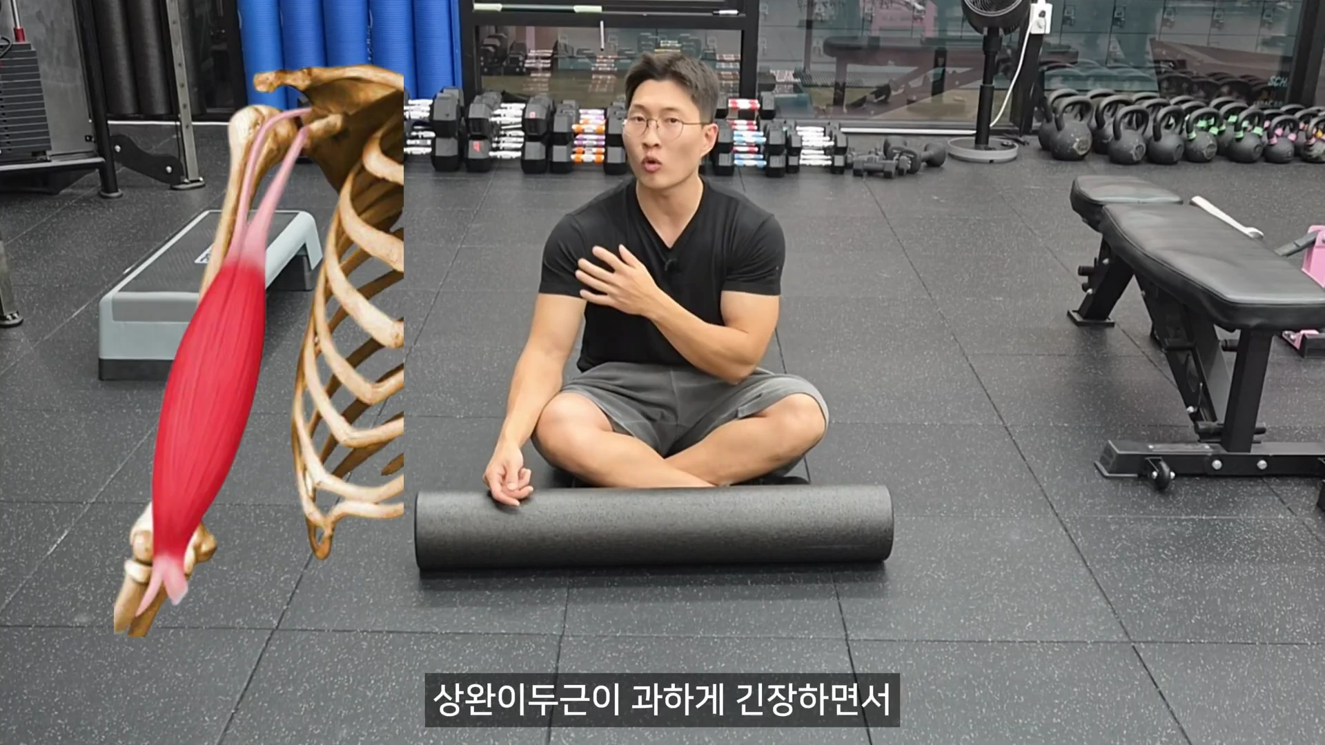 체육관 바닥에 앉아 있는 남성이 자신의 어깨 앞쪽을 손으로 가리키고 있으며, 화면 왼쪽에는 상완이두근의 위치를 보여주는 근골격계 그래픽이 합성되어 있다.