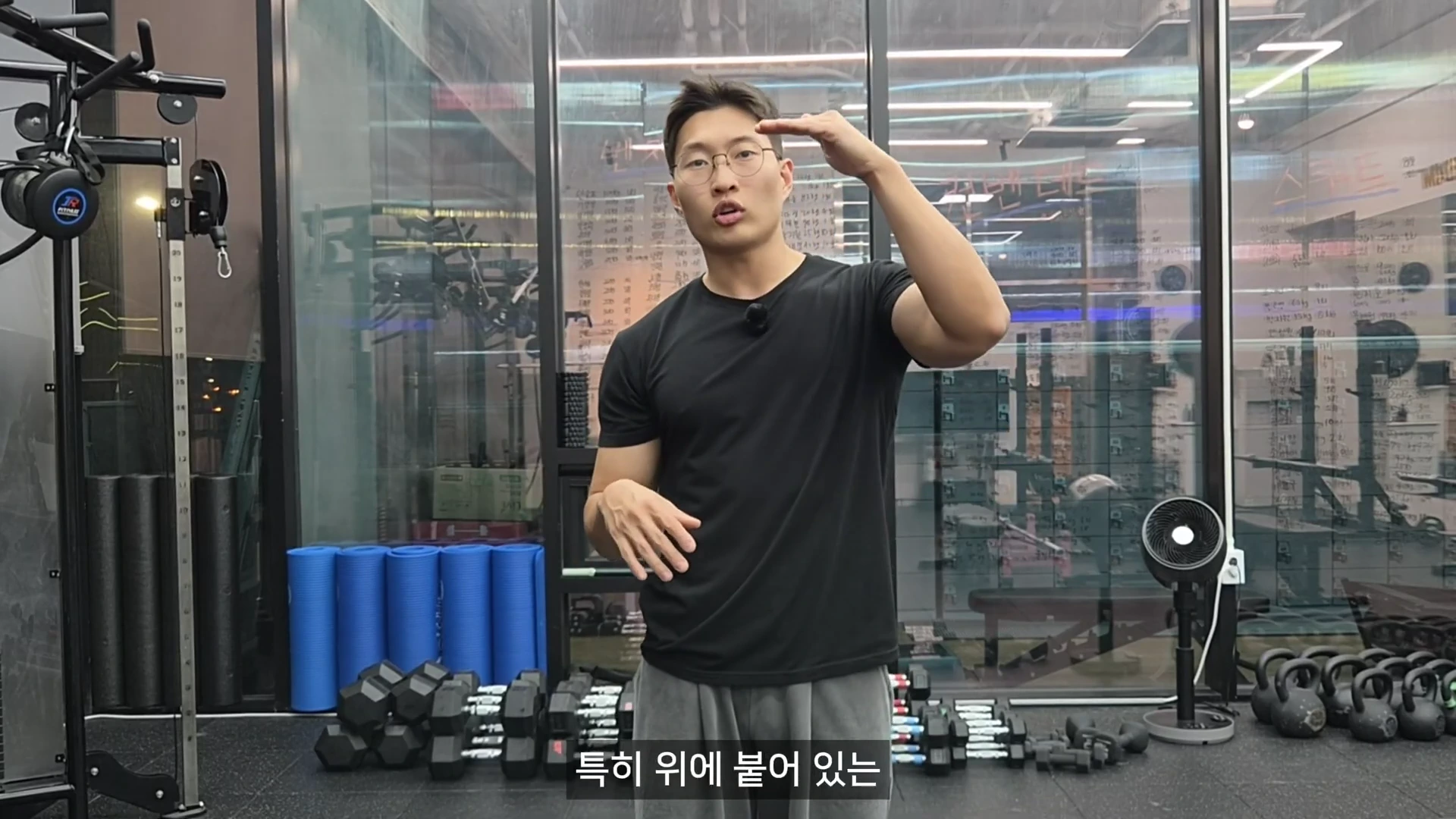 운동복 차림의 남성이 체육관에서 어깨 높이까지 팔을 올리며 동작을 설명하고 있다.