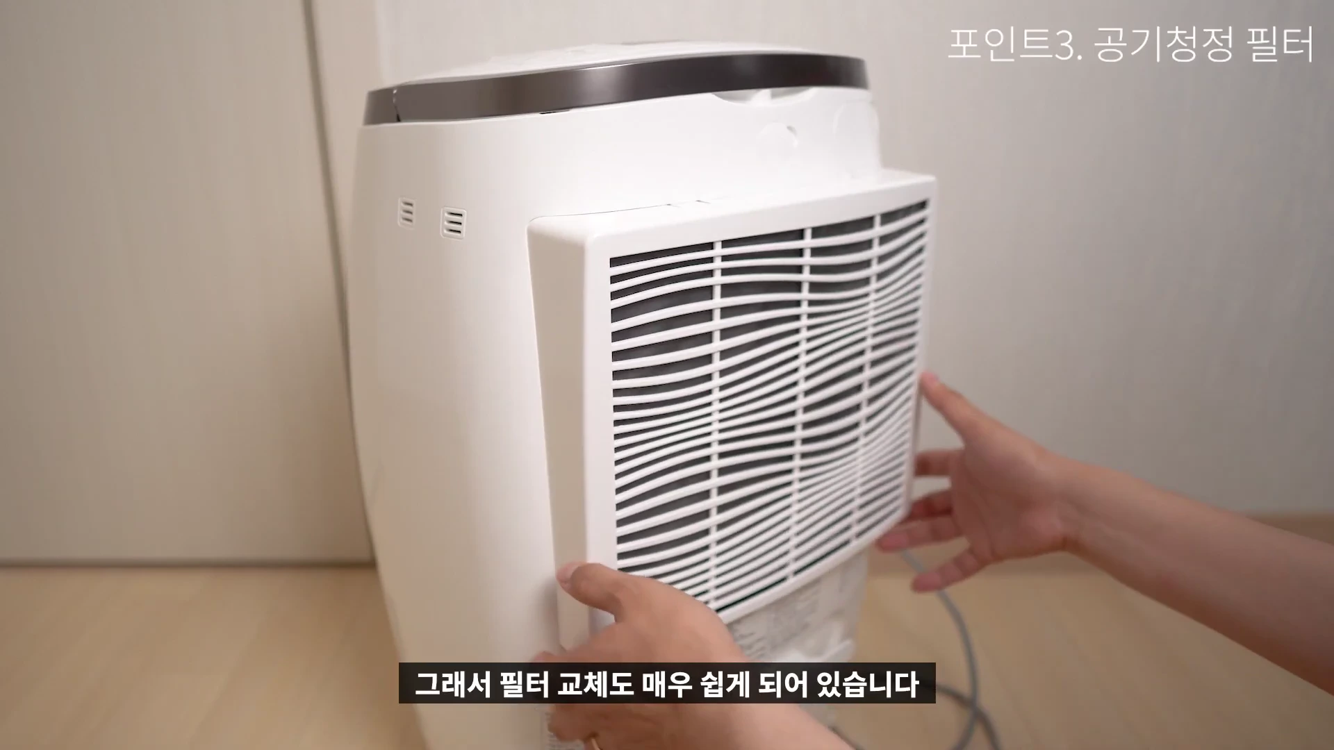 흰색 공기청정 제습기의 뒷면 필터 덮개를 양손으로 열고 있는 모습.