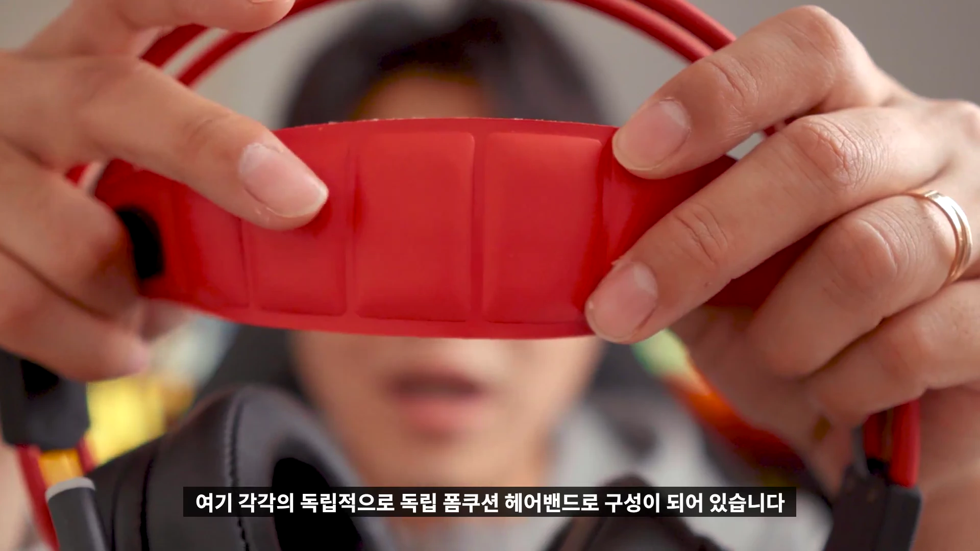 양손으로 게이밍 헤드셋의 빨간색 독립 폼 쿠션 헤어밴드 부분을 가까이 들어 올려 보여주고 있다.
