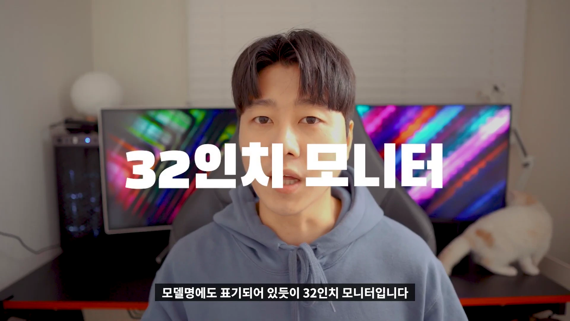한 남성이 카메라를 향해 말하고 있으며, 화면 중앙에는 '32인치 모니터'라는 큰 흰색 한글 자막이 떠 있고, 배경에는 두 대의 모니터가 설치된 책상이 보입니다.