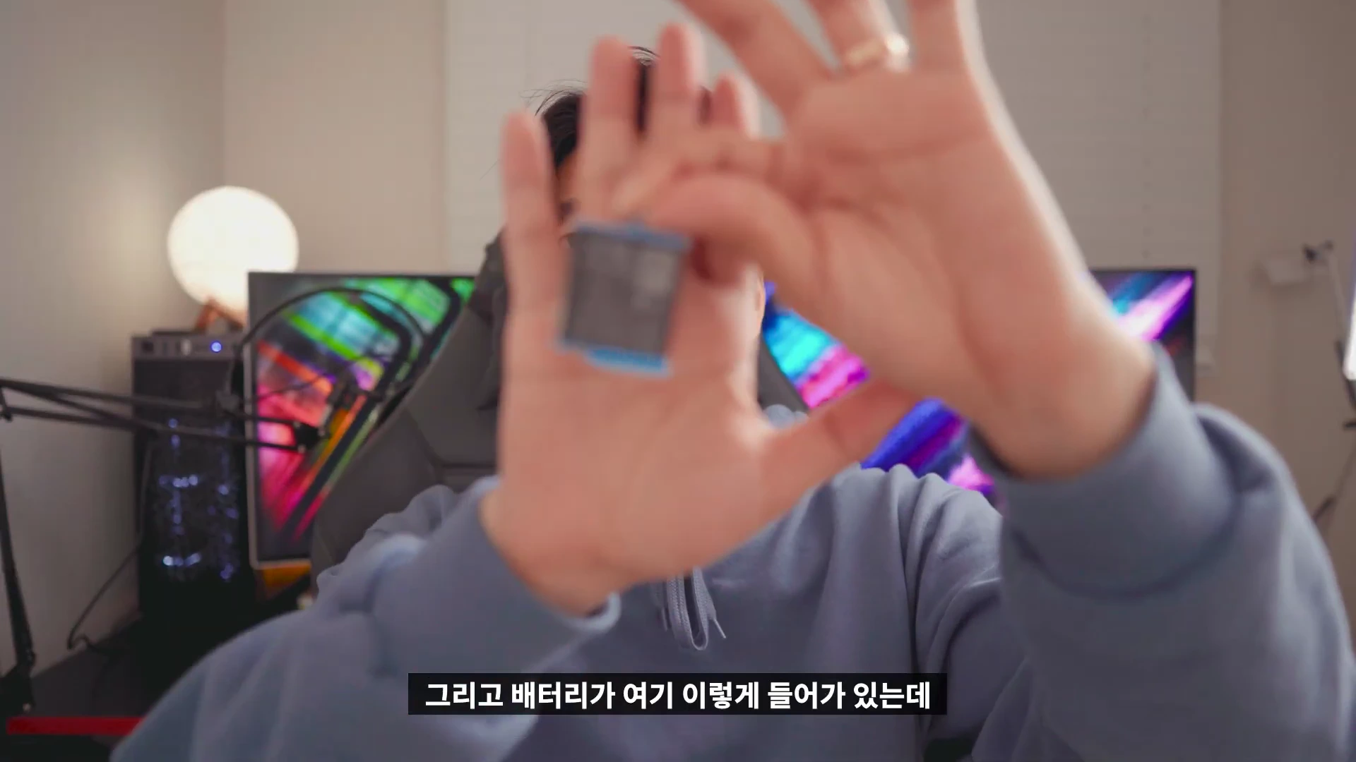 실내 스튜디오에서 한 남성이 손가락으로 고프로의 작은 직사각형 배터리를 들어 보이고 있는 모습