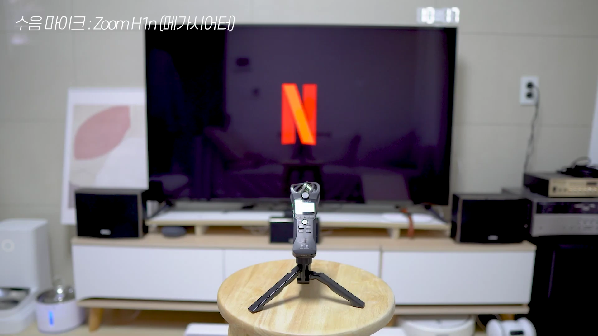 삼각대에 고정된 마이크가 거실의 TV 앞 의자 위에 놓여 있고, 배경인 TV 화면에는 넷플릭스 로고가 띄워져 있습니다.
