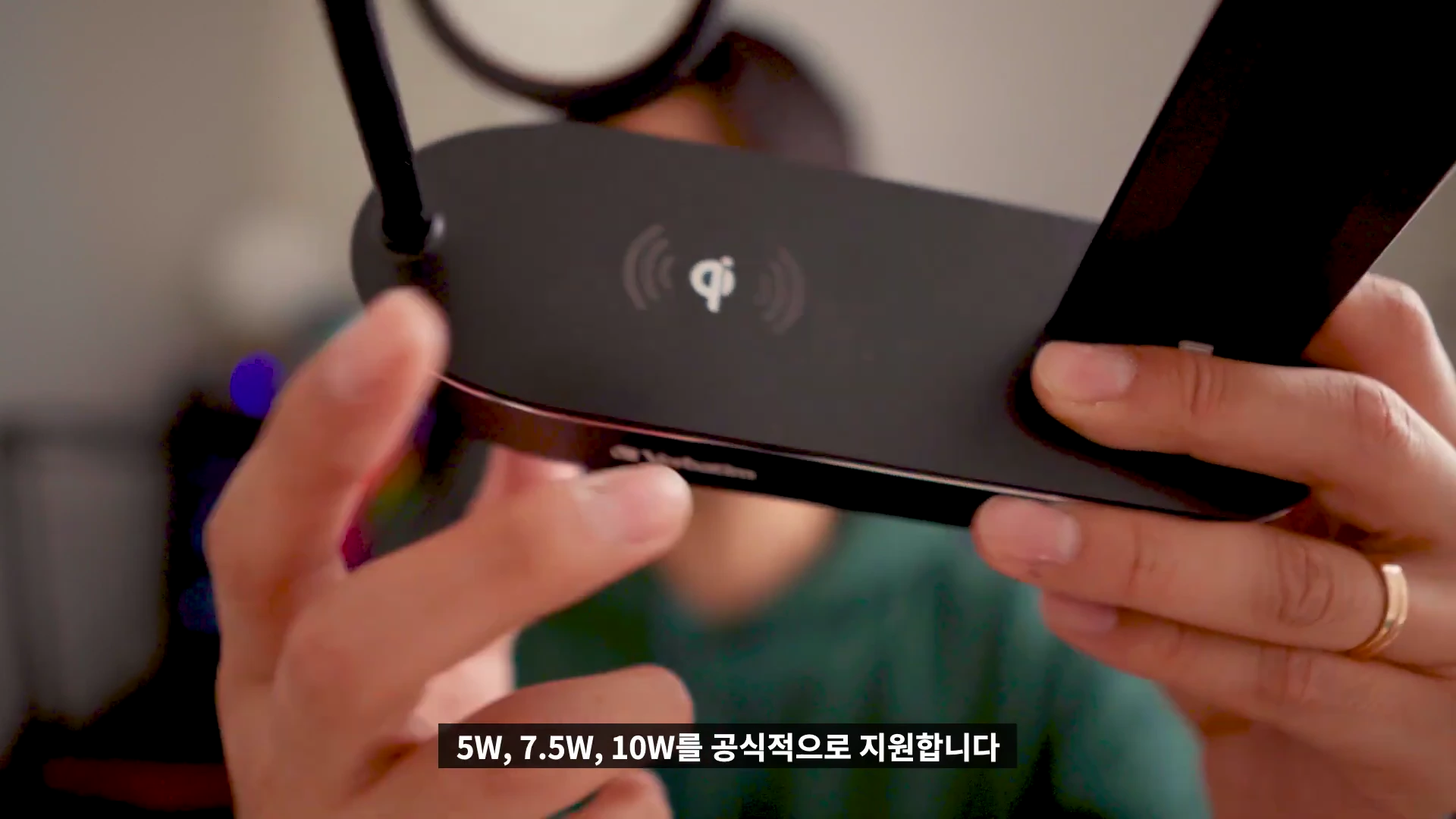 검은색 4-in-1 다기능 충전 스탠드 본체를 양손으로 들고 있는 모습이며 화면 하단에는 5W, 7.5W, 10W 출력을 지원한다는 자막이 표시되어 있습니다.