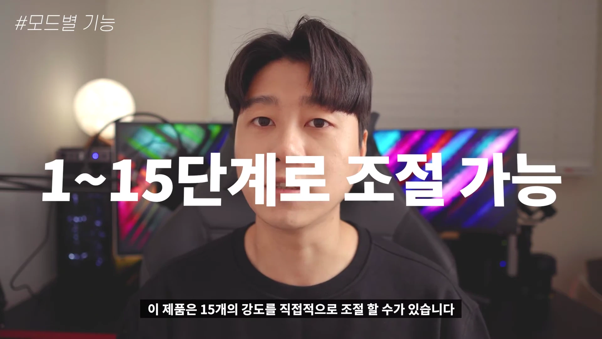 카메라를 정면으로 응시하는 남성 뒤로 화려한 조명이 켜진 모니터가 있는 방 안에서 촬영된 영상의 한 장면입니다. 화면 상단에는 '#모드별 기능'이라는 텍스트가, 중앙에는 '1~15단계로 조절 가능'이라는 큰 흰색 텍스트가 표시되어 있습니다.