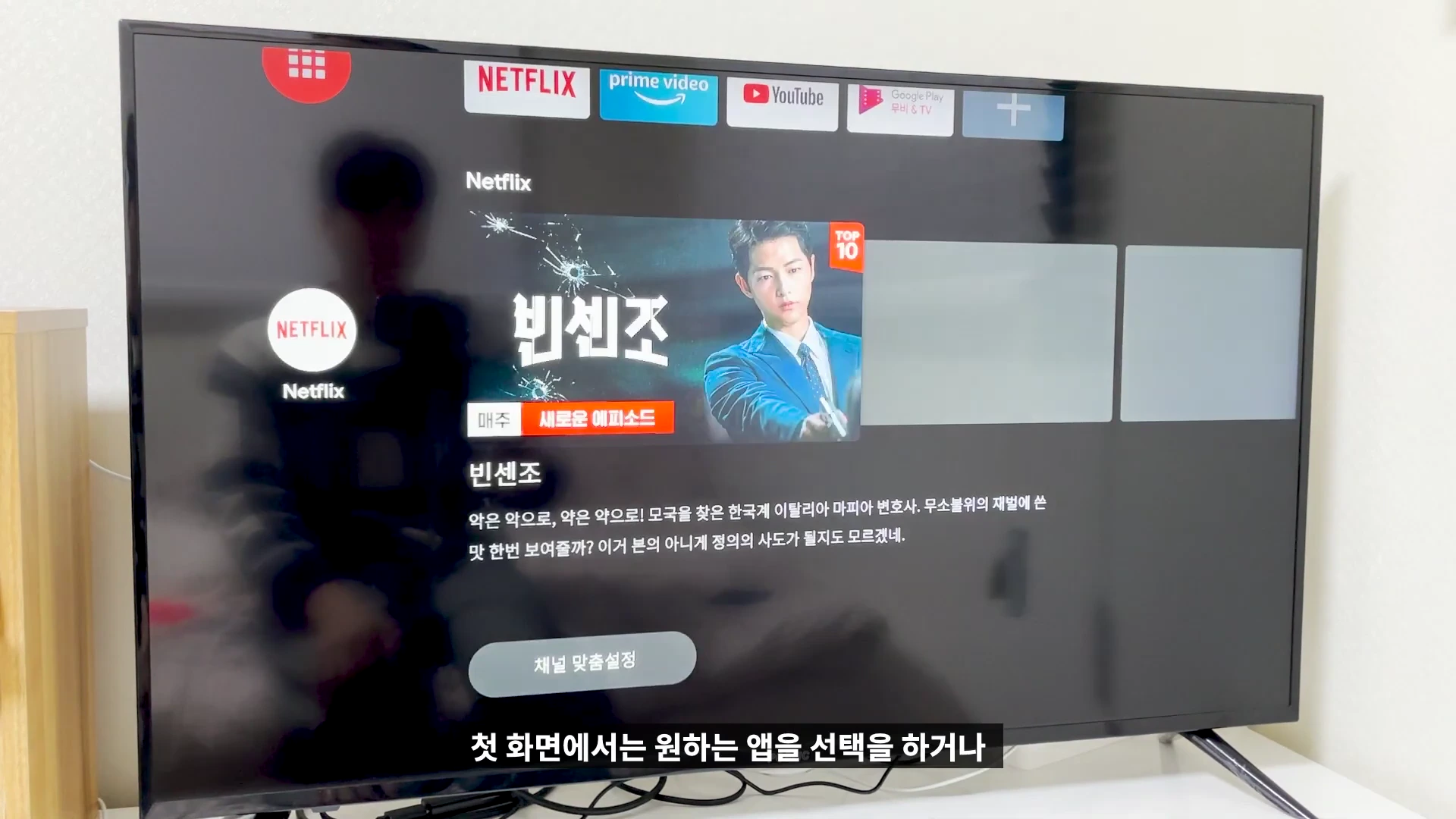 안드로이드 TV OS의 홈 화면이 출력되고 있는 TV 화면이며, 상단에는 넷플릭스, 유튜브 등 다양한 OTT 앱 아이콘이 정렬되어 있고, 화면 중앙에는 드라마 빈센조의 정보가 표시되어 있습니다.