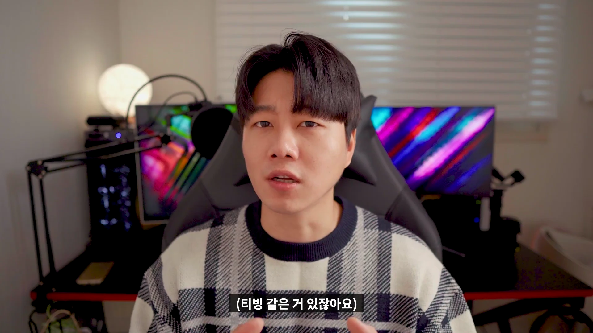 실내에서 격자무늬 니트를 입은 남성이 카메라를 정면으로 응시하며 설명하고 있고, 하단에는 '(티빙 같은 거 있잖아요)'라는 자막이 표시되어 있습니다.