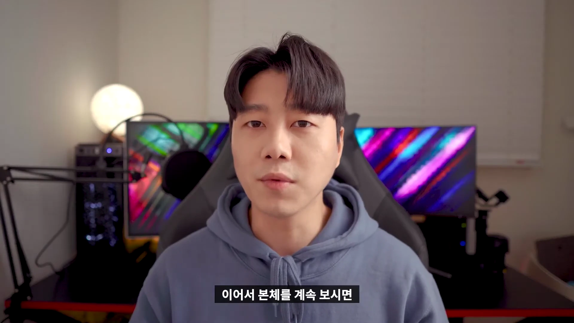 실내에서 후드티를 입은 남성이 정면을 바라보고 앉아 있는 모습이 담긴 화면 하단에 '이어서 본체를 계속 보시면'이라는 자막이 적힌 영상 프레임입니다.
