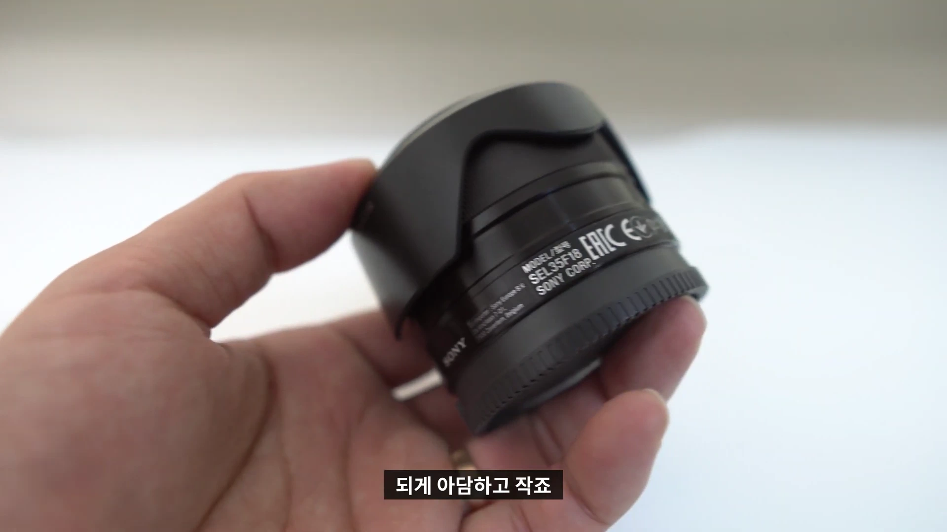 한 손으로 쥐고 있는 검은색 소니 35mm F1.8 렌즈의 모습
