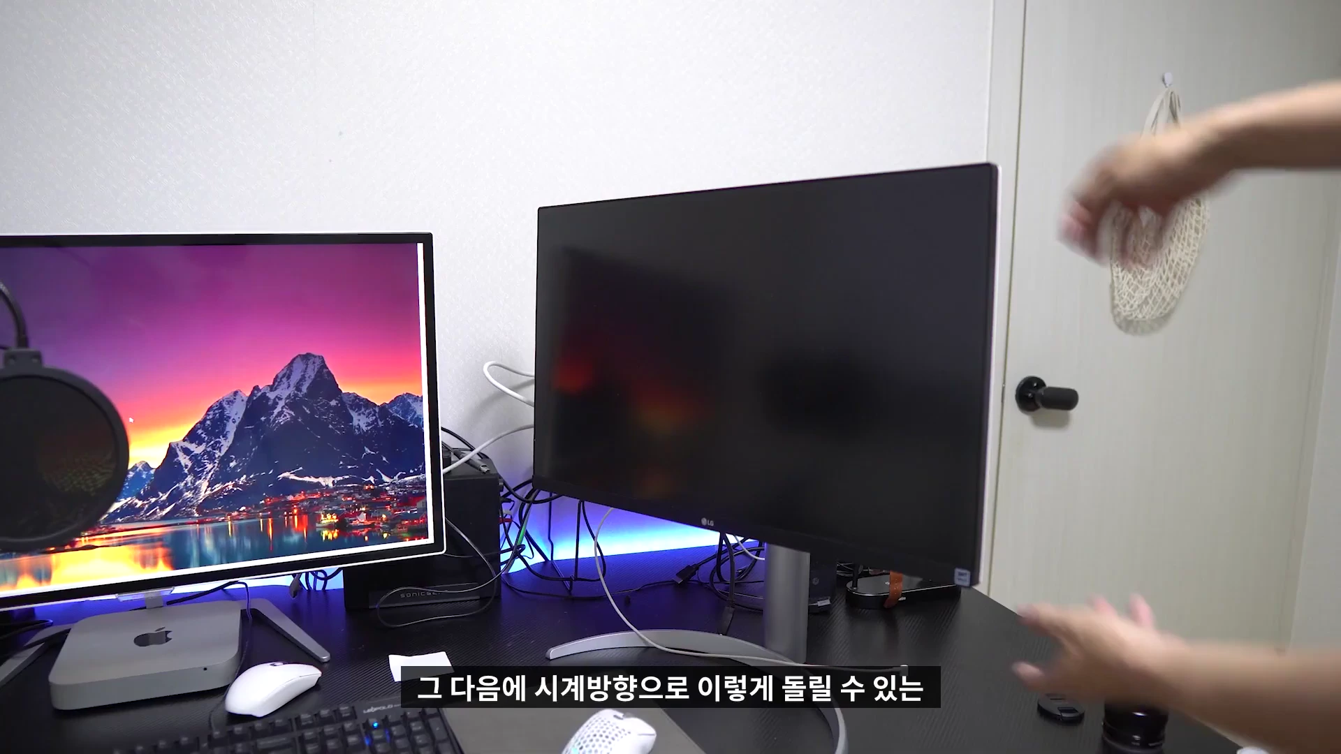 실내 책상 위에 설치된 두 대의 모니터 모습으로, 사용자의 손이 오른쪽에 배치된 모니터의 화면 방향을 세로로 돌리는 피벗 기능을 시연하고 있다.