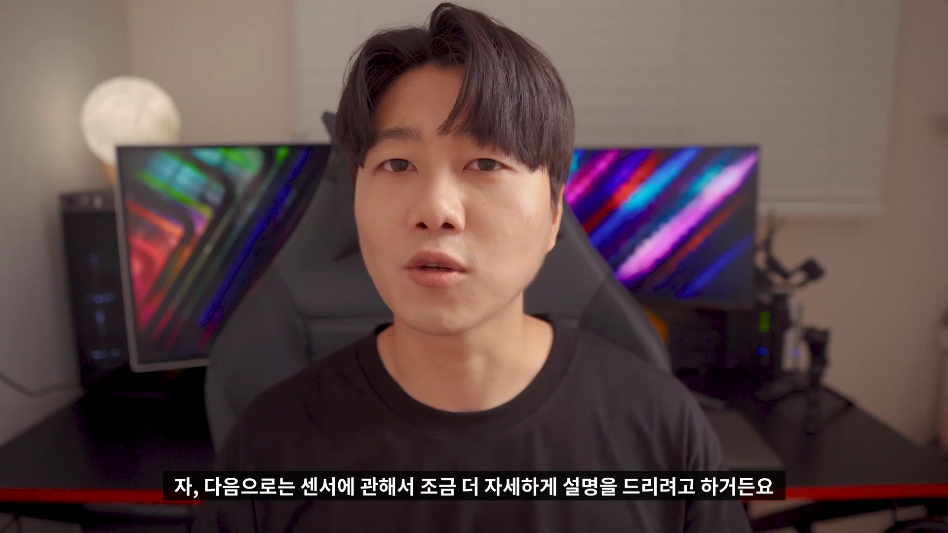 검은색 티셔츠를 입은 한 남성이 실내 작업 공간에서 카메라를 정면으로 바라보며 설명하고 있는 영상 캡처 화면입니다.
