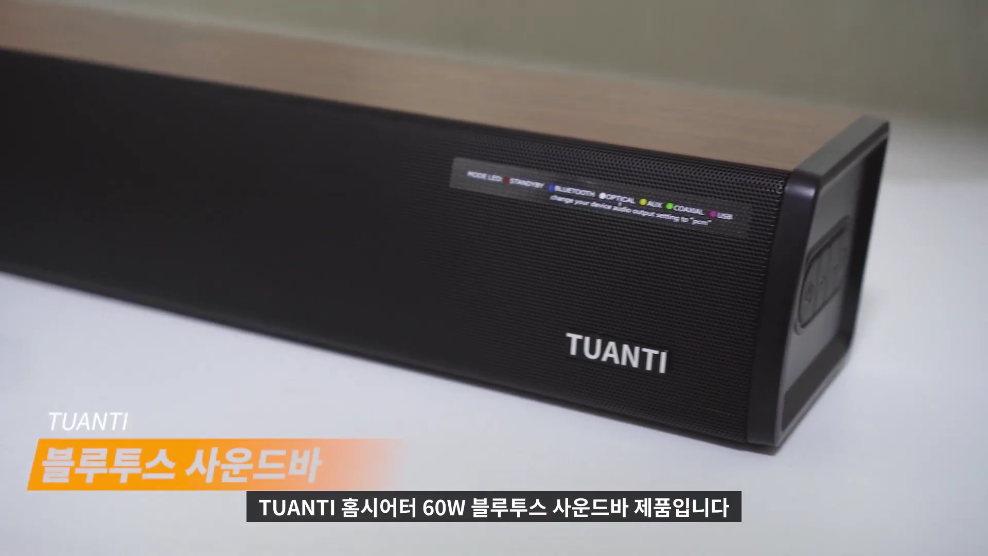 나무 무늬 상단과 검은색 그릴이 특징인 TUANTI 브랜드의 사운드바 본체가 흰색 배경에 놓여 있고, 전면 오른쪽에는 입력을 나타내는 LED 상태 표시등과 브랜드 로고가 보입니다.