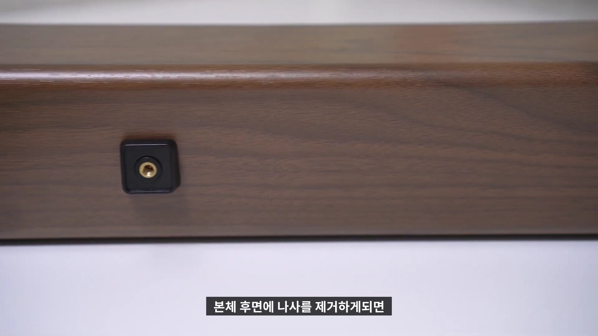 나무 무늬가 있는 사운드바 본체 후면의 나사 구멍이 클로즈업되어 보입니다.