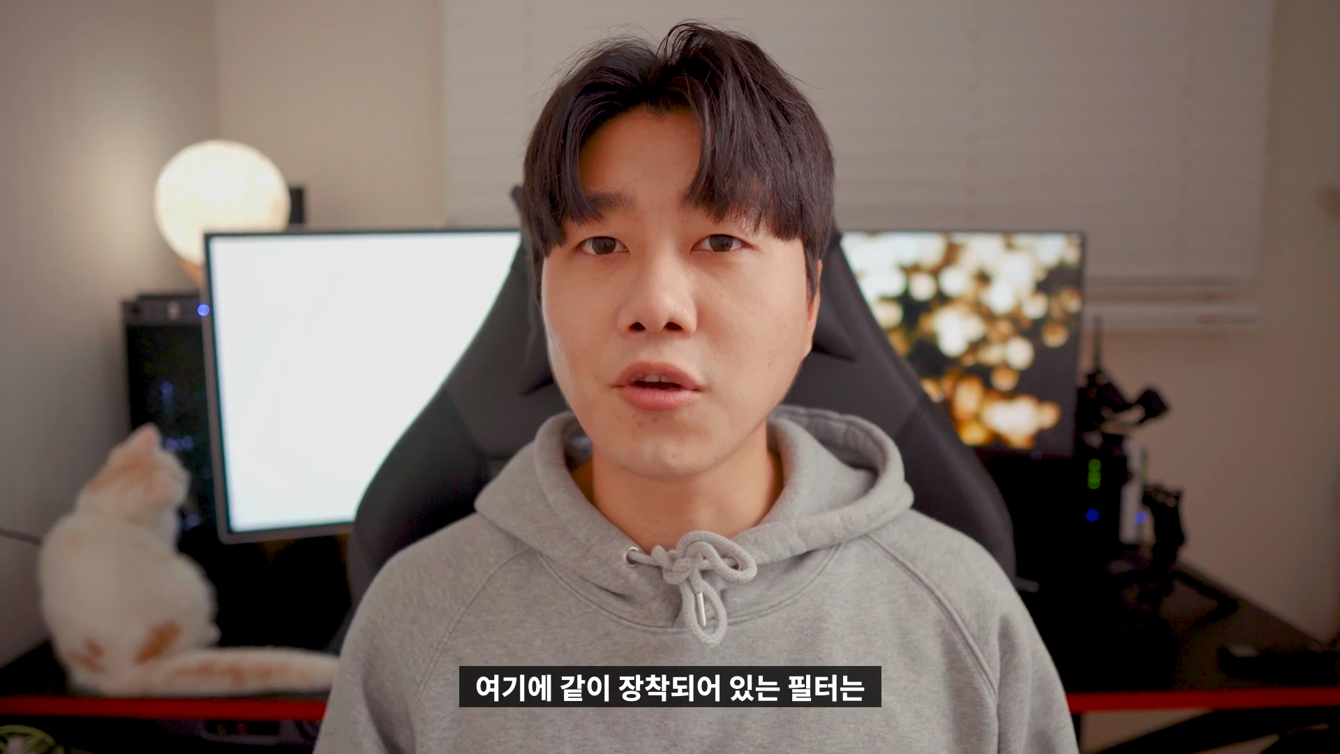 실내 스튜디오에서 회색 후드 티를 입은 남성이 정면을 응시하며 이야기하고 있으며, 화면 하단에는 흰색 자막이 표시되어 있습니다.