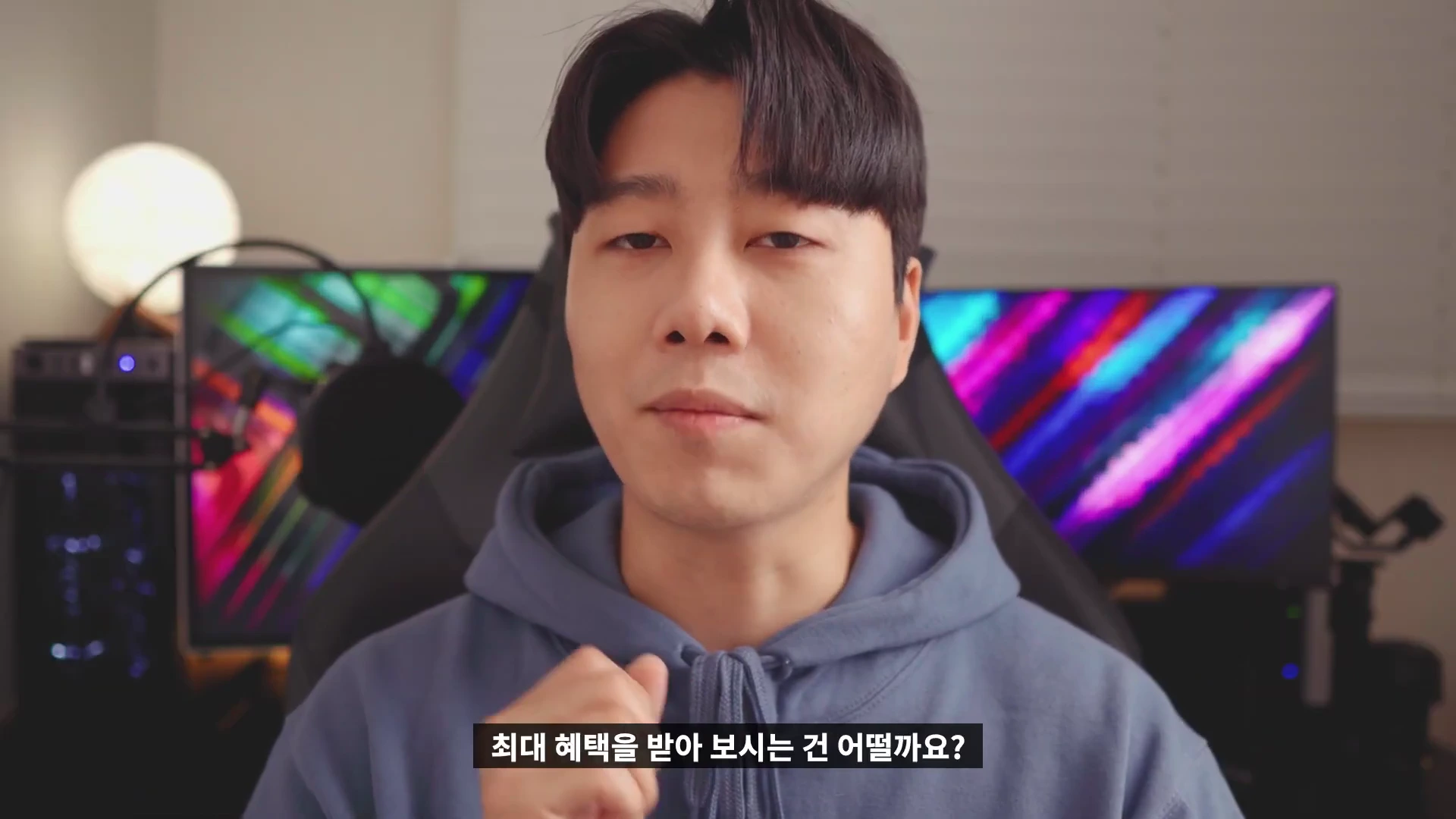 실내에서 후드티를 입은 남성이 카메라를 응시하며 이야기하고 있으며, 화면 하단에는 '최대 혜택을 받아 보시는 건 어떨까요?'라는 자막이 표시되어 있습니다.