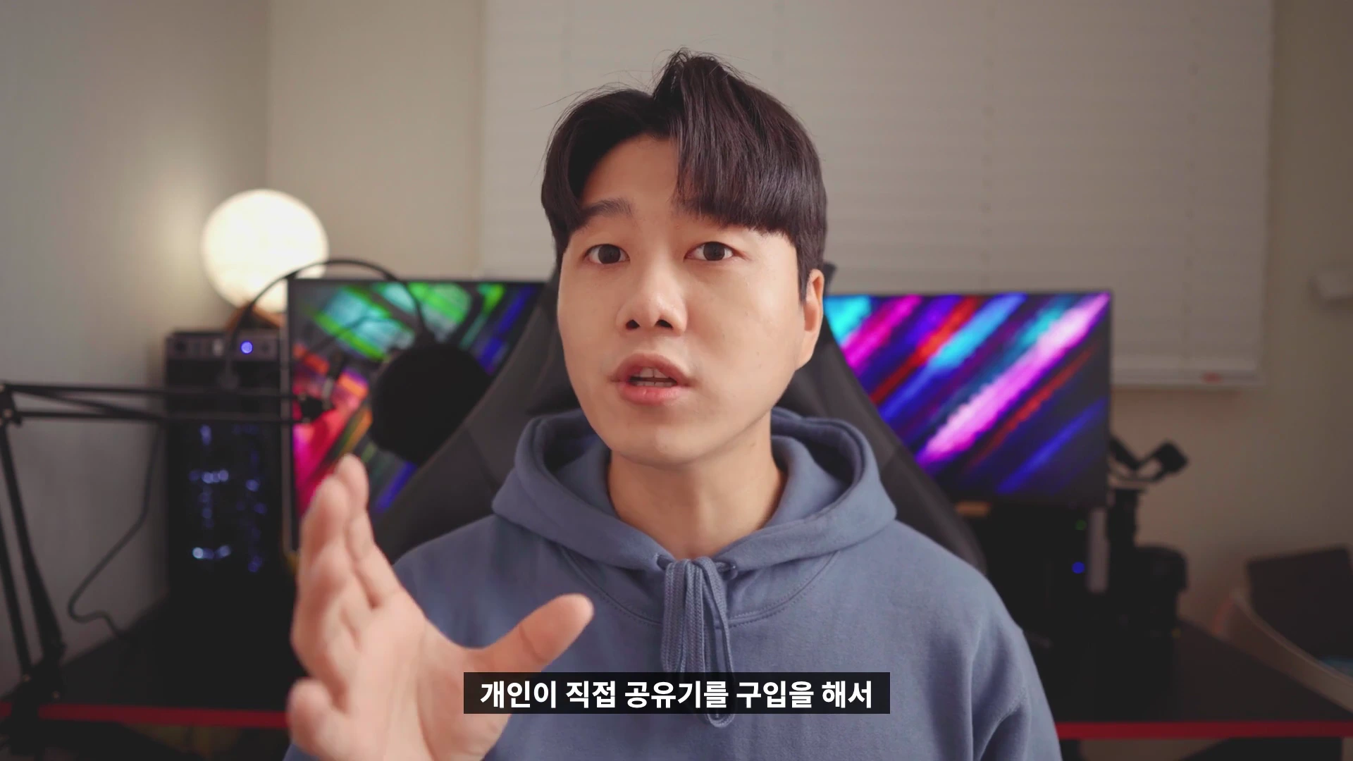 실내 책상에 앉아 설명하고 있는 젊은 남성의 상반신 화면으로, 하단에는 '개인이 직접 공유기를 구입을 해서'라는 한국어 자막이 표시되어 있습니다.