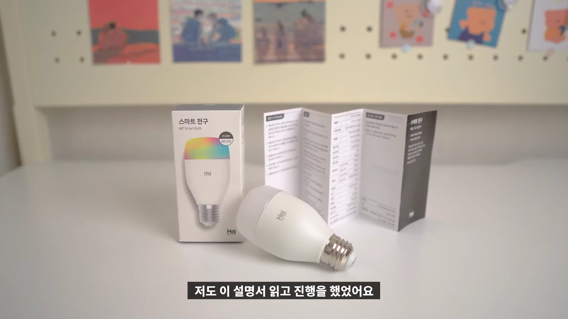 흰색 테이블 위에 놓인 스마트 전구 제품 패키지와 본체, 그리고 펼쳐진 제품 설명서가 정면으로 보입니다.