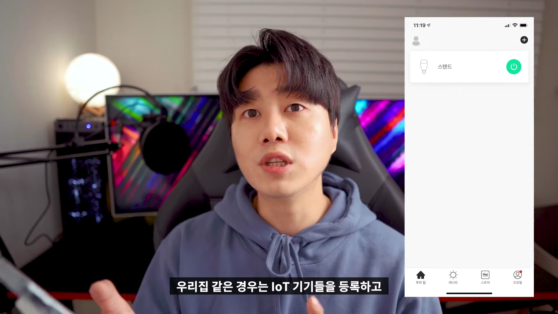 안경을 쓴 남성이 카메라를 보며 설명하고 있으며, 오른쪽에는 헤이홈 전용 앱의 '우리 집' 탭 화면이 스마트폰 인터페이스 형태로 떠 있다.