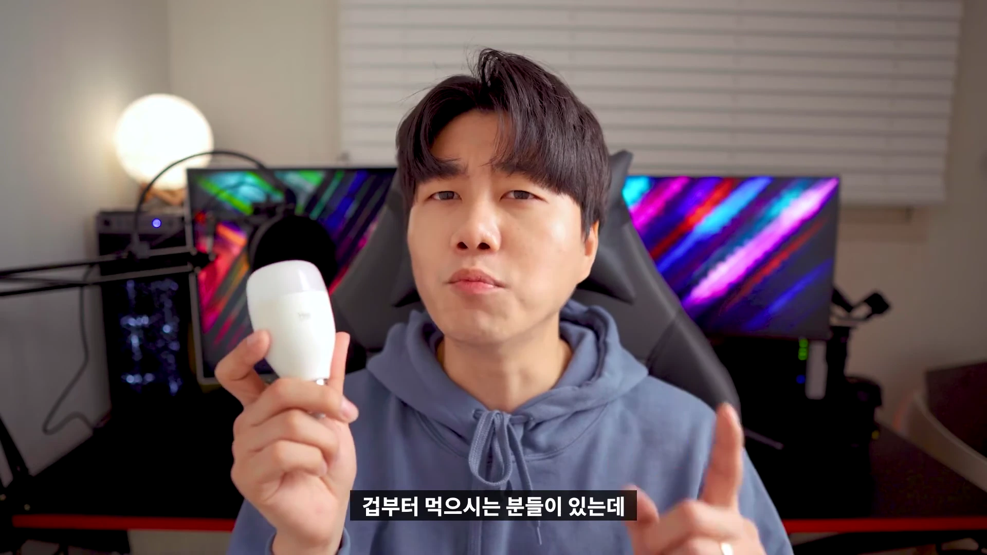 실내에서 후드티를 입은 남성이 손에 스마트 전구를 들고 카메라를 보며 설명하고 있는 모습