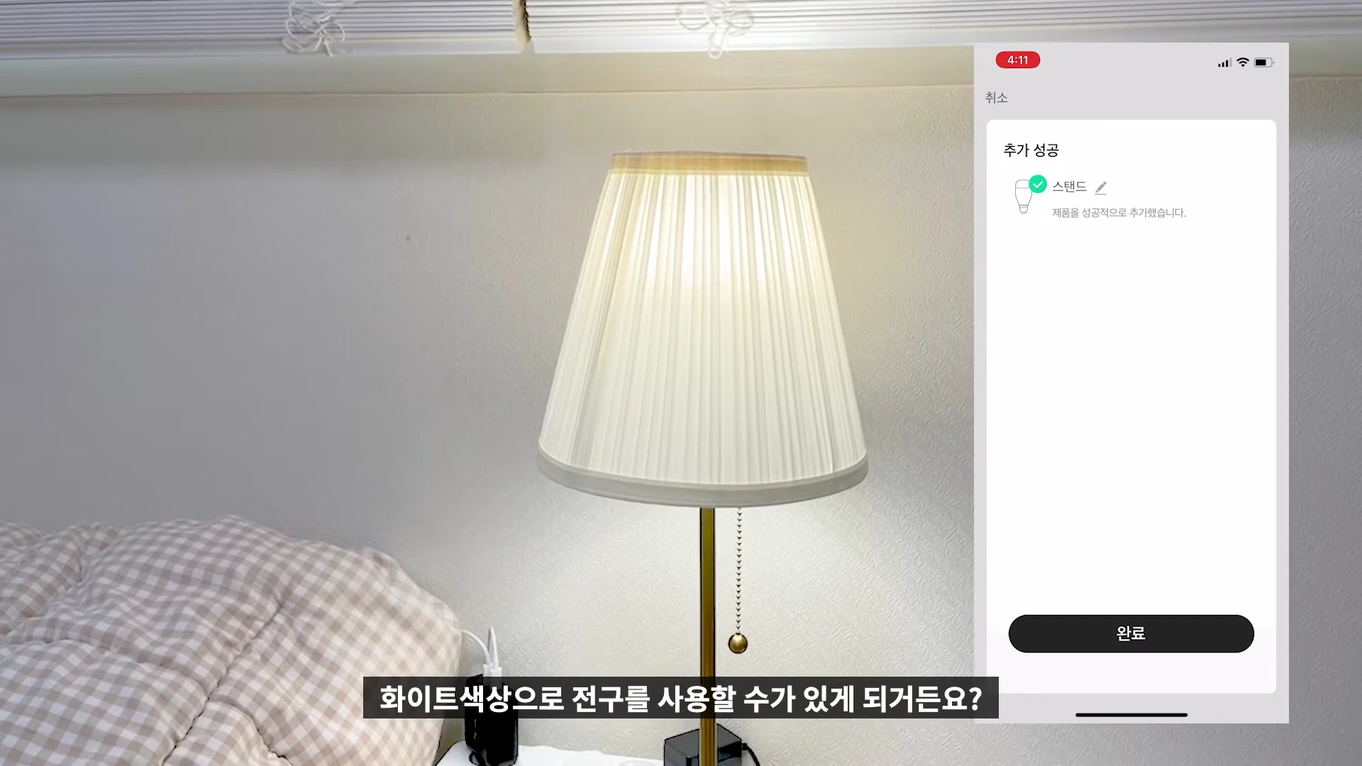 스마트폰 화면에 '추가 성공' 메시지와 스탠드 아이콘이 표시된 모습과 함께 옆에 켜진 조명 스탠드가 배치된 영상 화면.