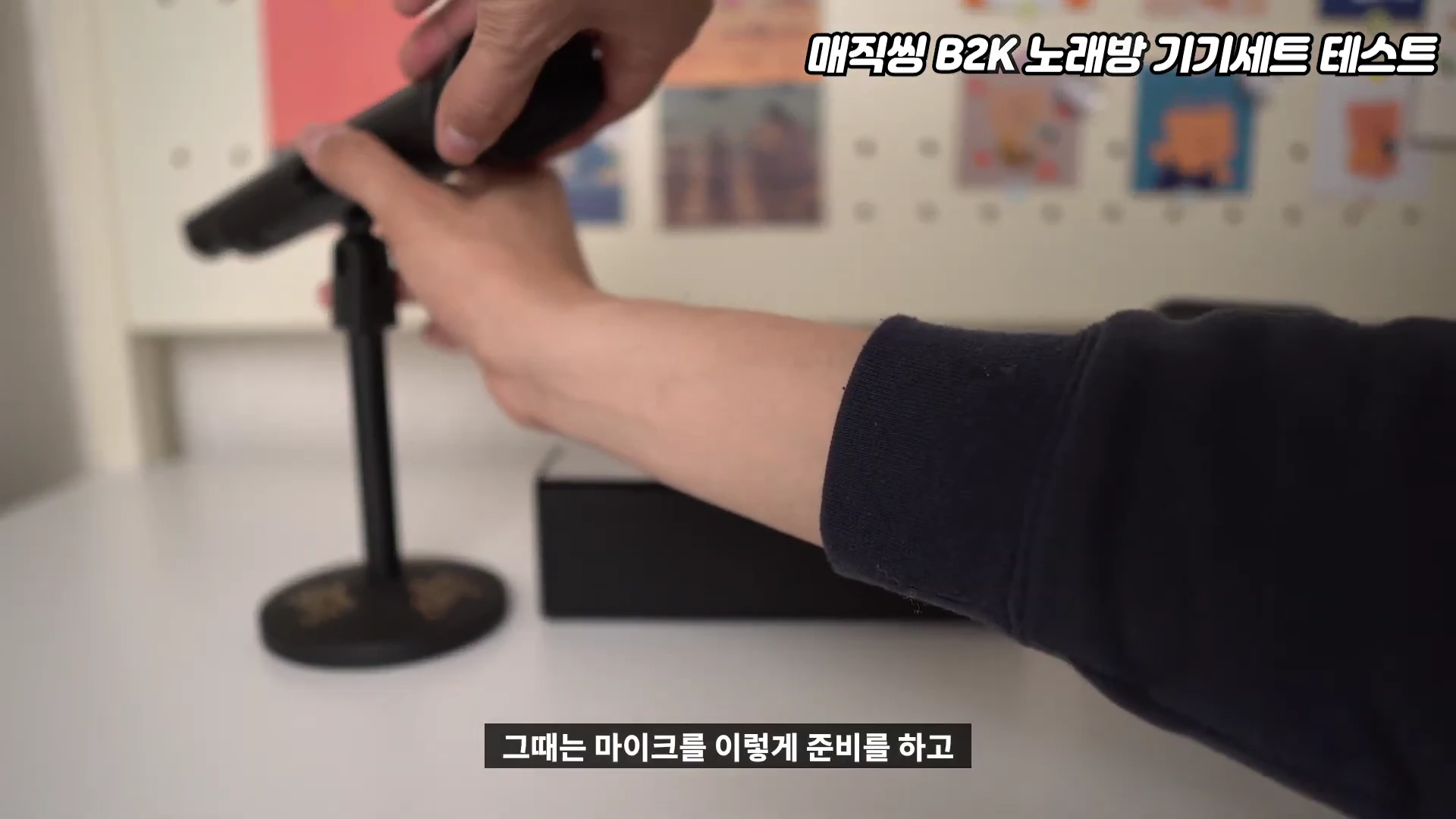 손이 마이크를 스탠드에 거치하는 모습이 담긴 클로즈업 영상 캡처 화면