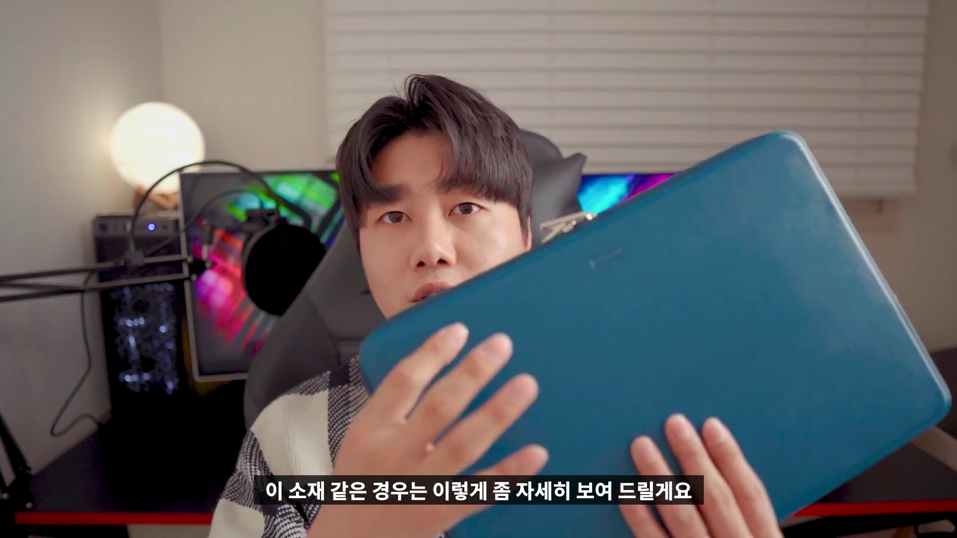 한 남성이 카메라를 향해 짙은 청록색 가죽 노트북 파우치를 들어 보이며 소재를 보여주고 있다.
