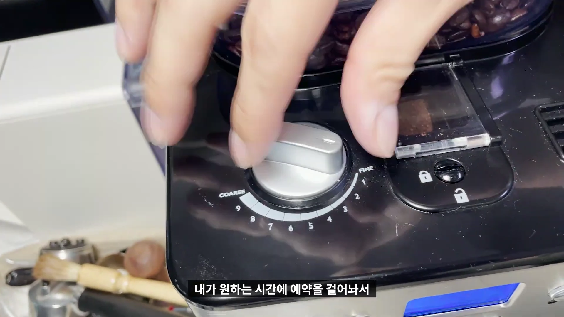 커피 머신 상단에 위치한 원두 분쇄도 조절 다이얼을 손가락으로 돌려 굵기를 조정하는 모습입니다.