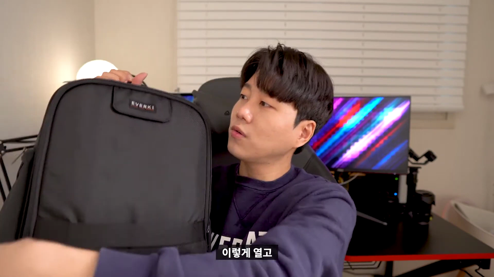 실내에서 한 남성이 검은색 노트북 백팩을 손으로 들어 보이며 설명하고 있는 모습