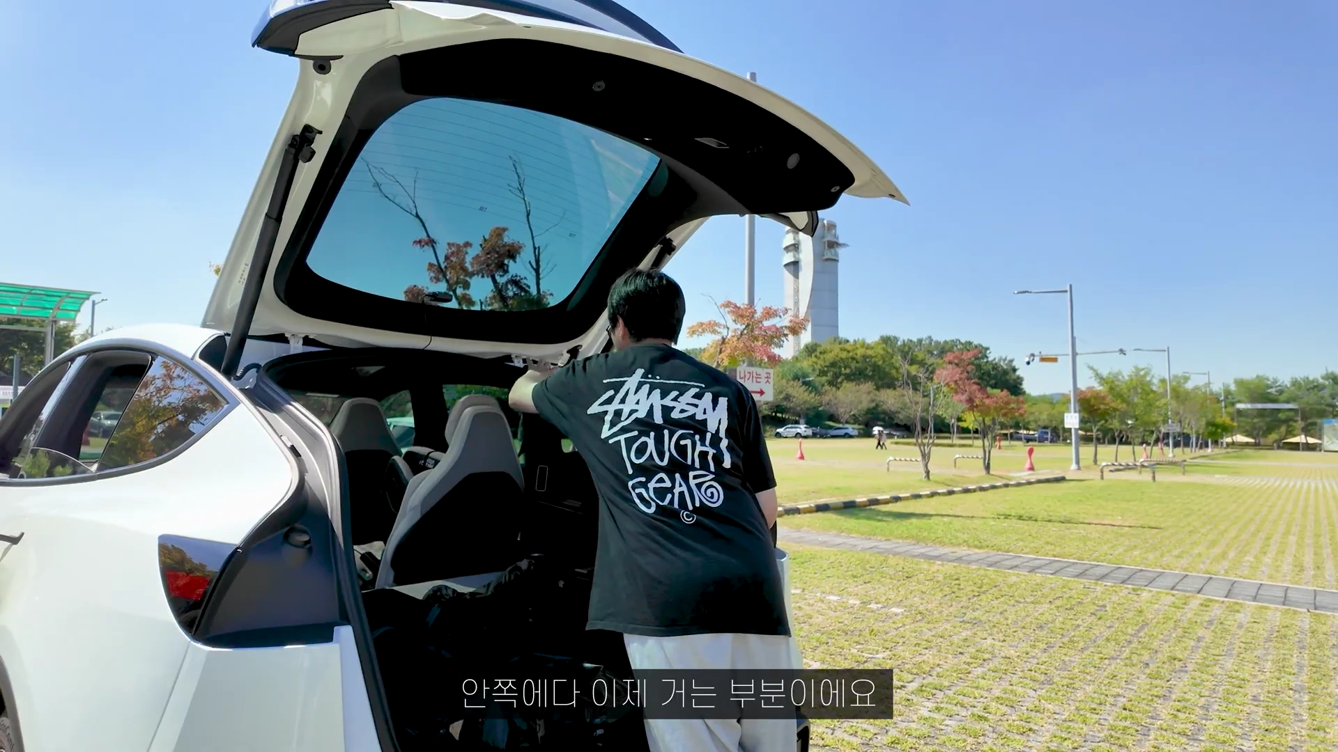 한 남성이 주차된 차량의 열린 트렁크 안쪽 프레임에 꼬리텐트 고리를 거는 모습
