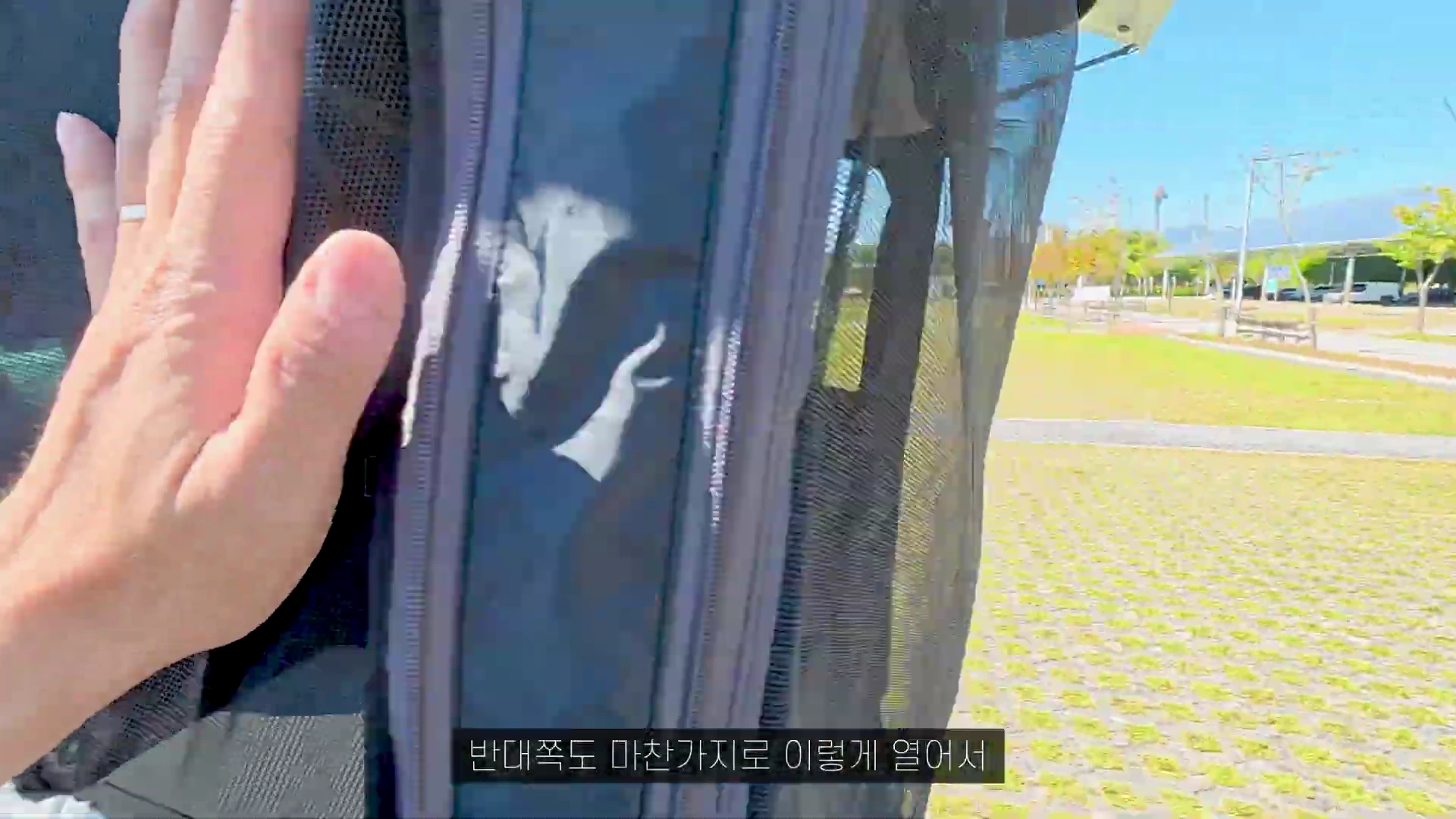 차량 꼬리텐트의 메쉬 소재 방충망과 가림막을 손으로 만지는 모습이 보이는 캠핑장 풍경.