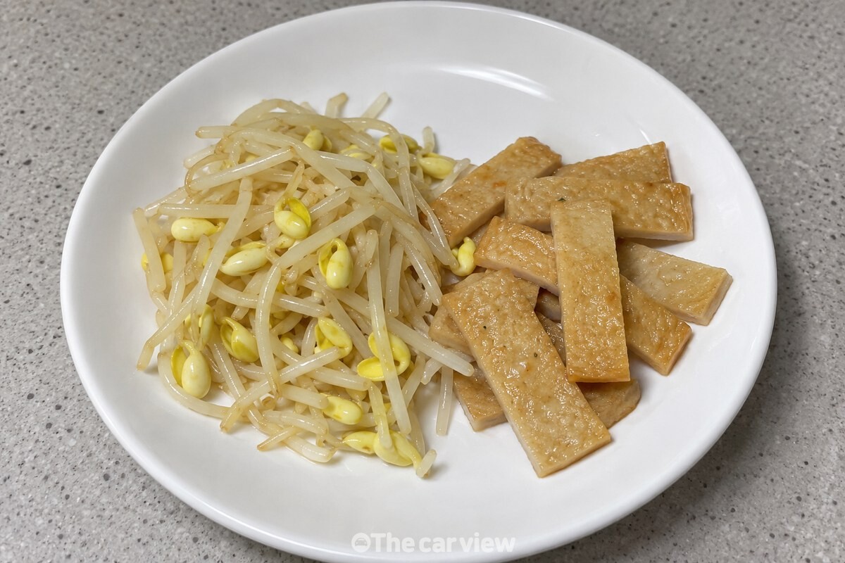 익으면서 양이 줄어든 콩나물과 썰어 둔 어묵이 깨끗한 접시에 놓여 있는 모습 / 기사 이해를 돕기 위한 생성형 이미지