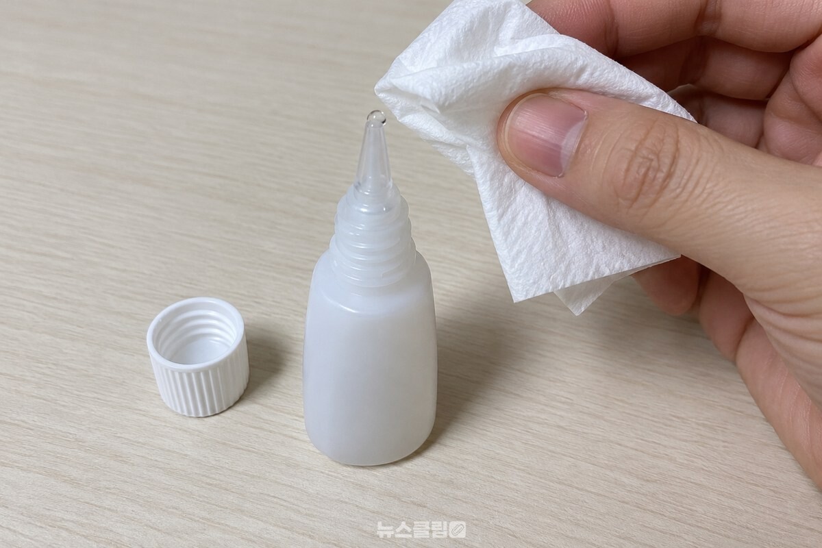 깨끗한 책상 위에서 노즐을 위로 세운 순간접착제 용기의 입구를 접은 휴지로 닦는 모습. / 기사 이해를 돕기 위한 생성형 이미지