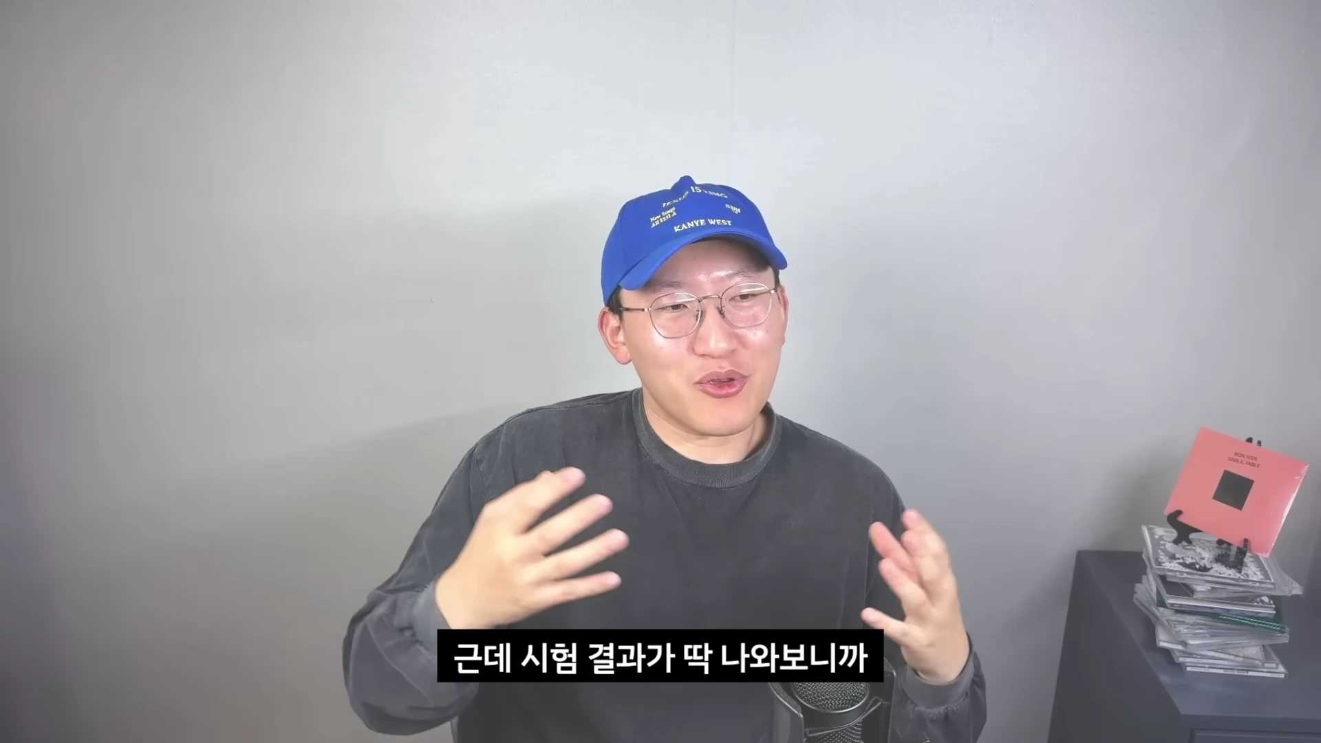 파란색 모자와 안경을 쓴 남성이 마이크 앞에서 손짓하며 이야기를 나누고 있는 유튜브 영상 화면.