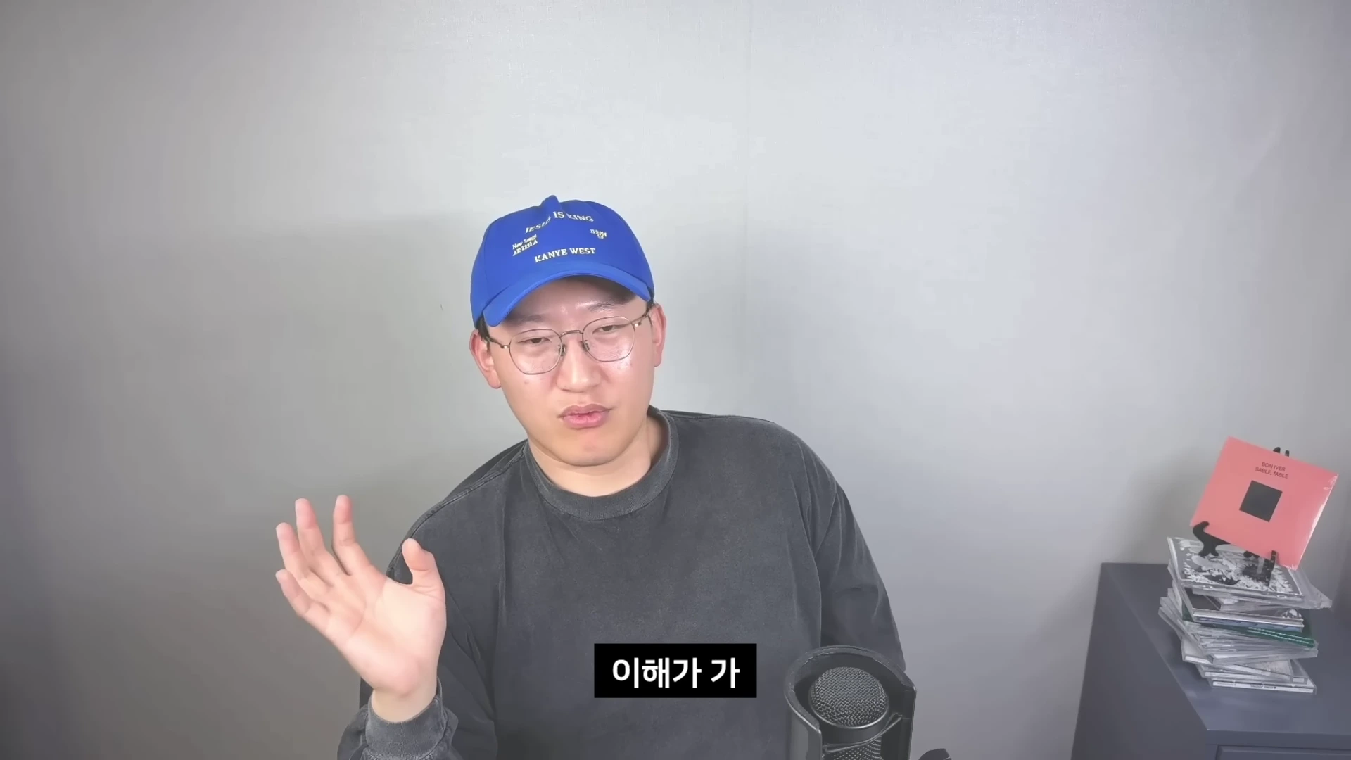푸른색 야구 모자를 쓴 남성이 마이크 앞에서 손을 들어 올리며 대화하고 있는 모습.