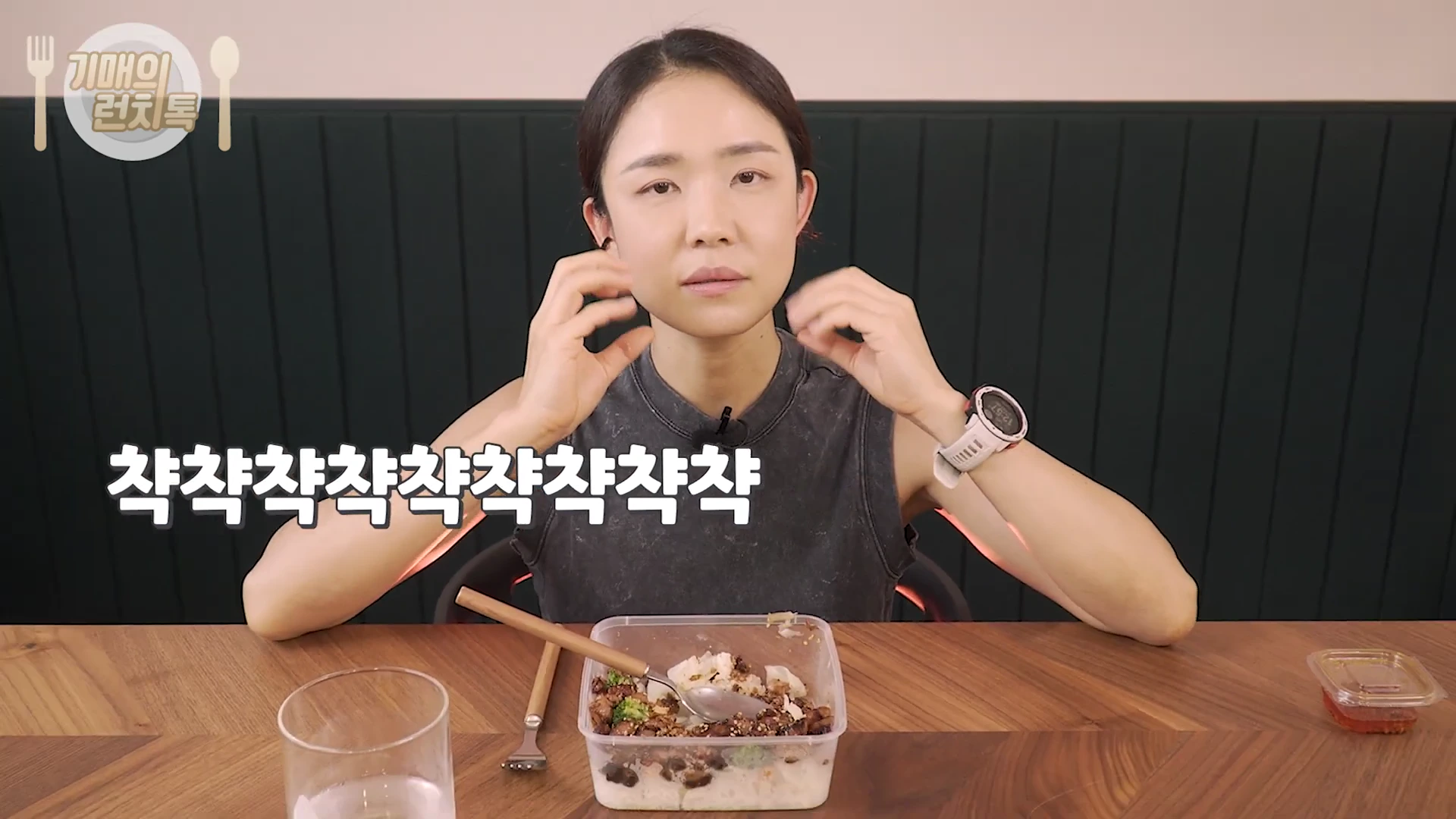한 여성이 테이블 앞에 앉아 배달 용기에 담긴 덮밥을 앞에 두고 손짓하며 이야기를 나누고 있는 모습