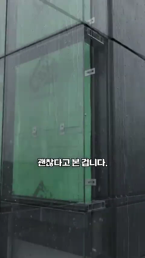 빗줄기가 맺힌 건물 외벽의 유리 패널 사이로 녹색 내장재가 덧대어진 틈새가 보이는 모습